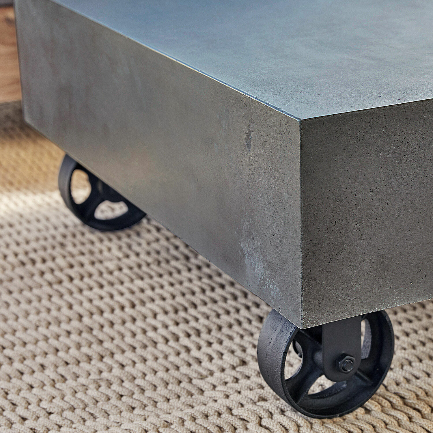 Grauer Beton-Couchtisch auf schwarzen Metallrollen auf beigem Teppich