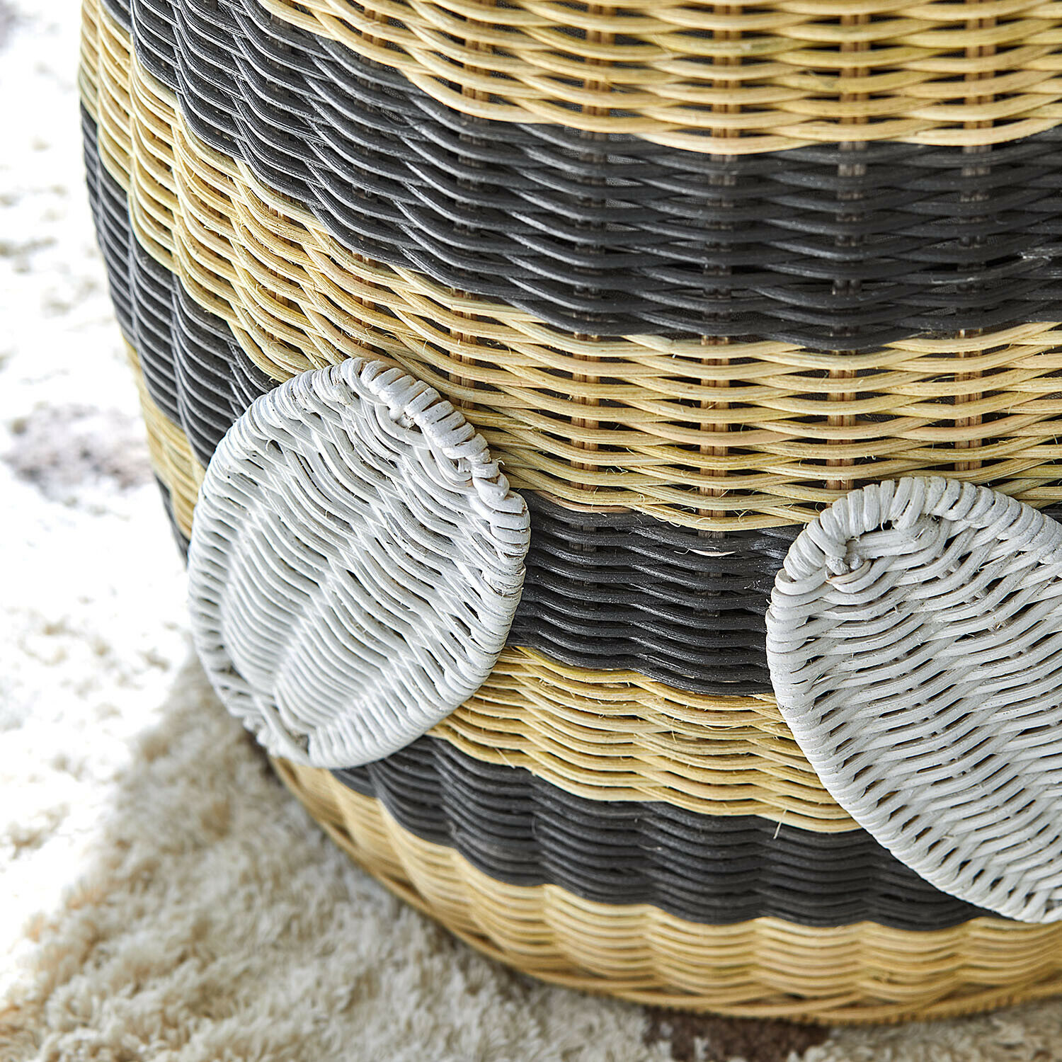 Geflochtener Korb in Beige-Schwarz mit weißen runden Elementen auf Teppich, Wohnaccessoire