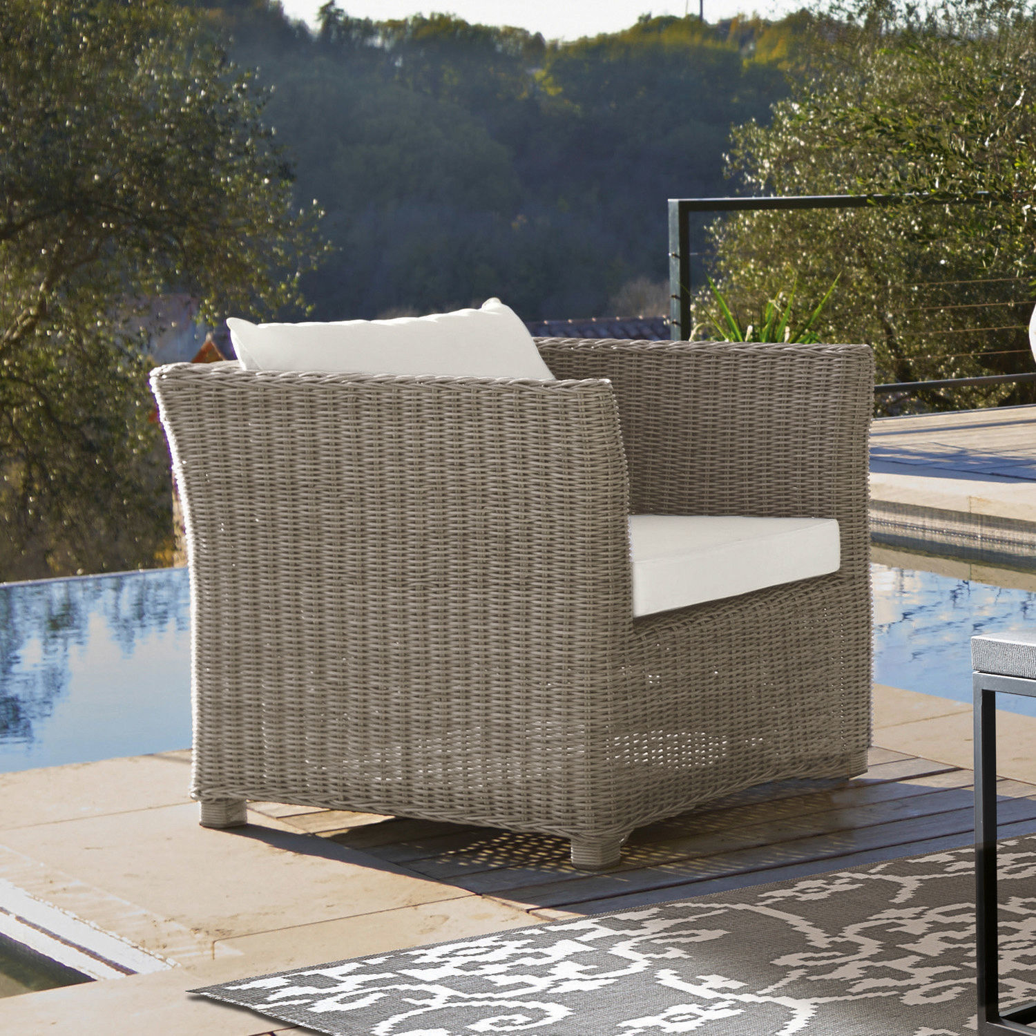 Gartenfauteuil aus grauem Rattan mit weißem Kissen, ideal zum Entspannen auf der Terrasse am Pool