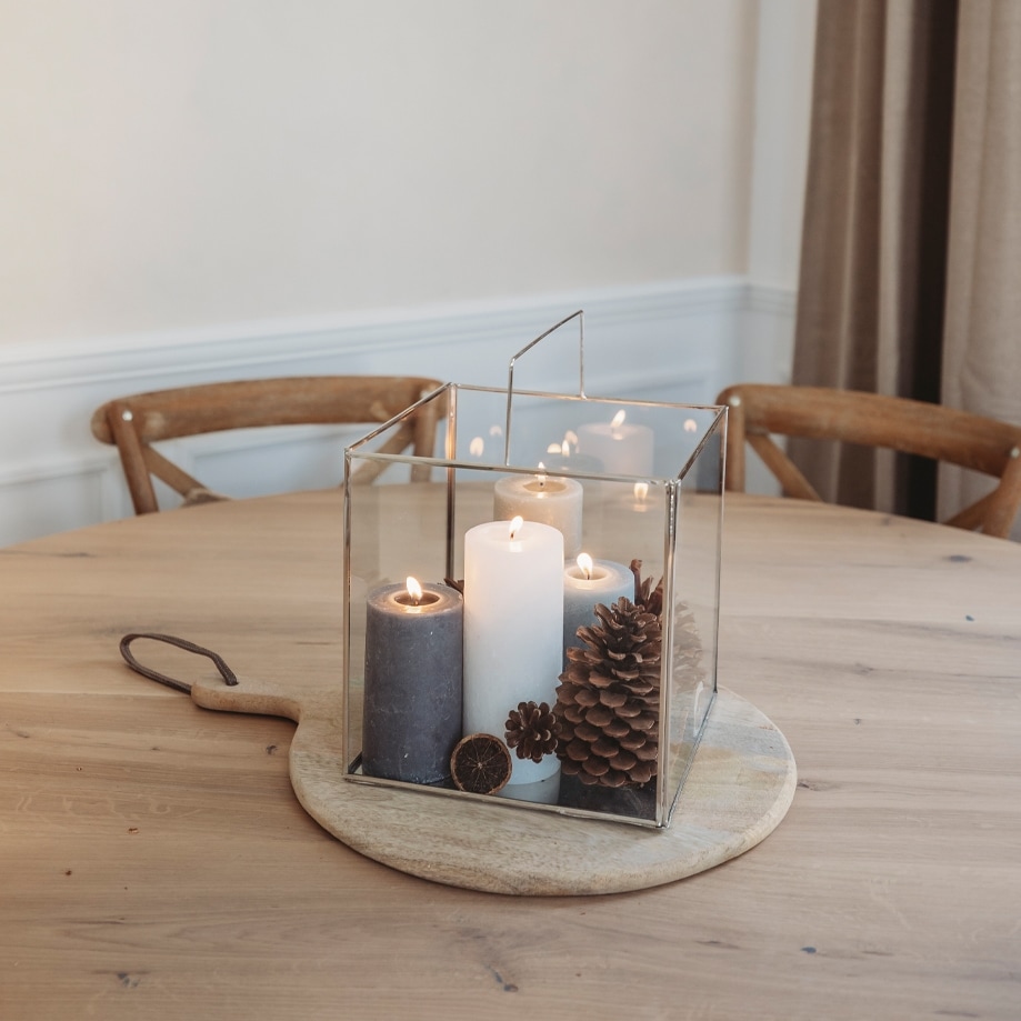 Glaslaterne mit drei Kerzen und Kiefernzapfen auf Holzbrett als Weihnachtsdekoration auf Tisch
