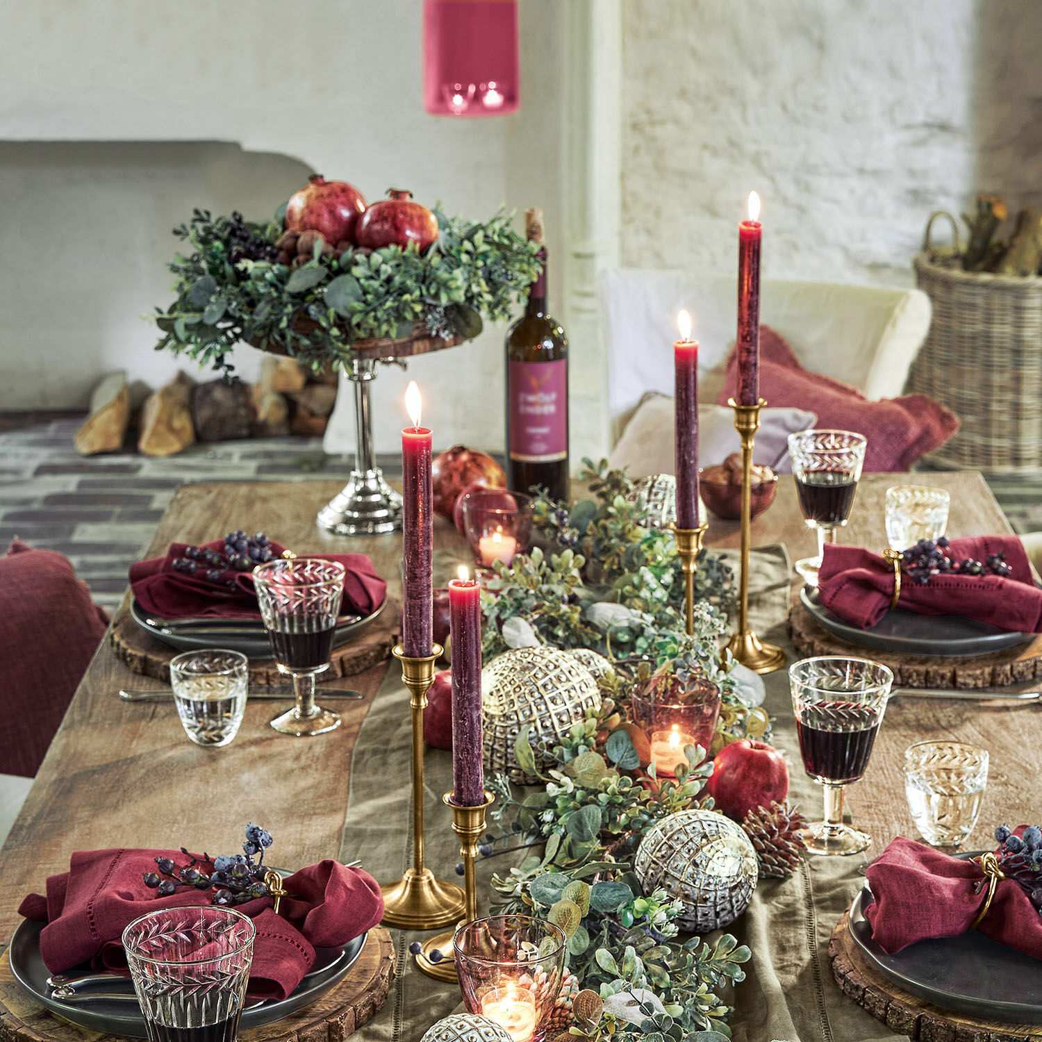 Elegante Tischdekoration mit bordeauxfarbenen Kerzen, grünen Zweigen und roten Granatäpfeln