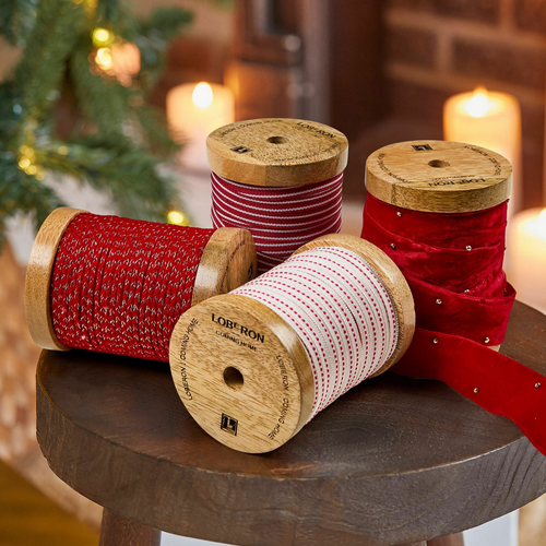 Vier Holzspulen mit roten und weißen Dekobändern für festliche Weihnachtsdekorationen
