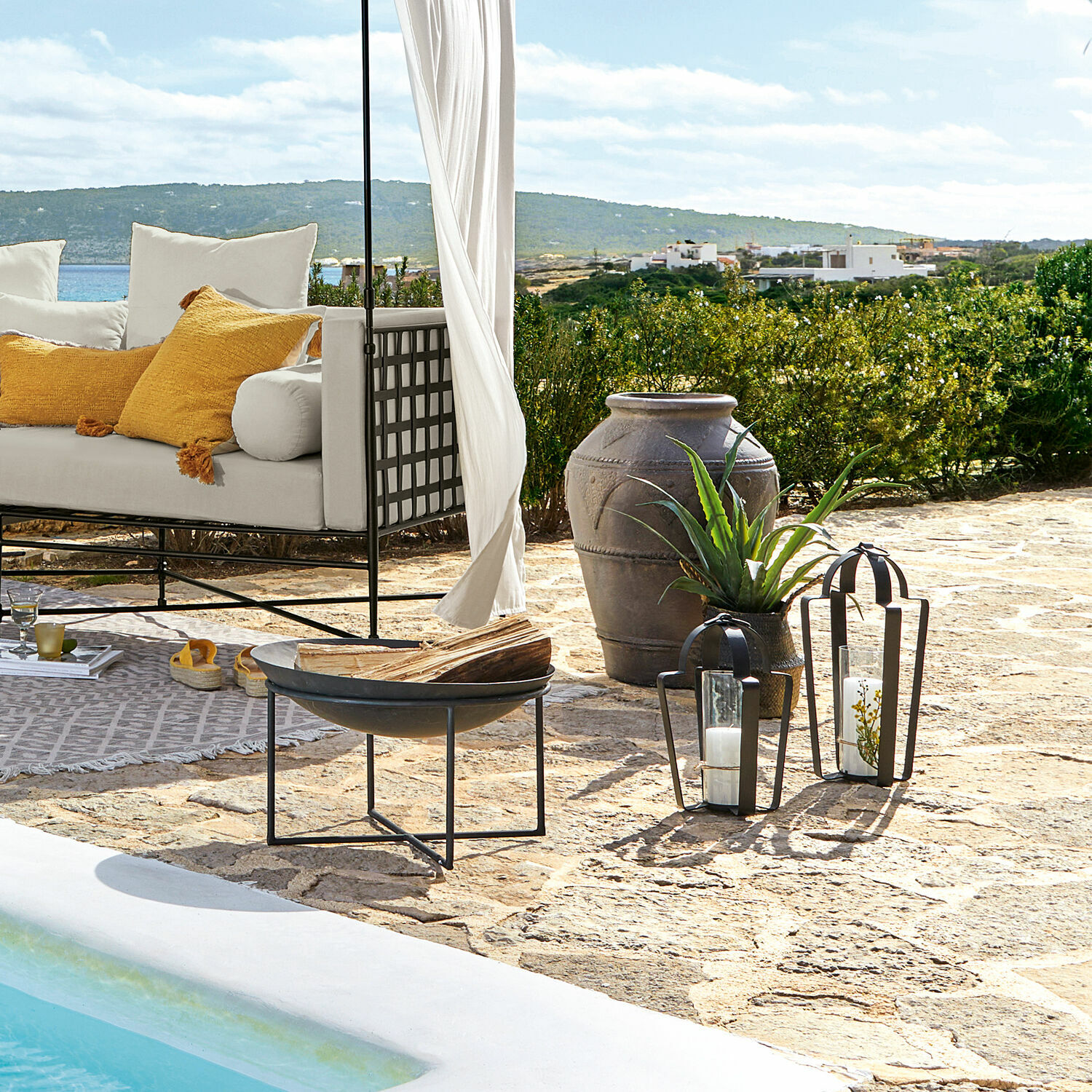 Gemütlicher weißer Sessel mit gelben Kissen auf steinerner Terrasse am Pool mit Meerblick