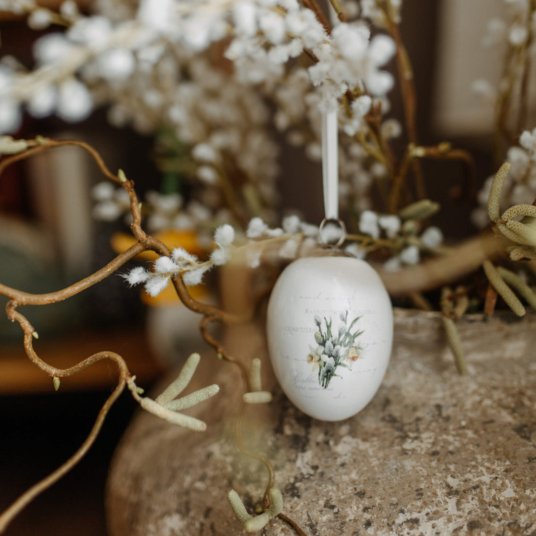Weiße Keramik-Ostereier-Dekoration mit Blumenmotiv an dekorativem Zweig