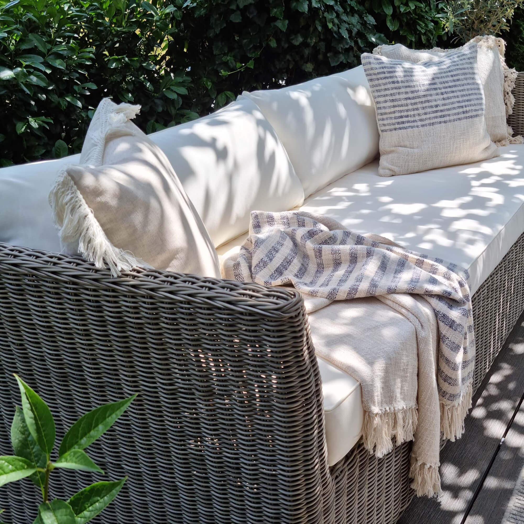 Gartensofa aus grauem Rattan mit cremefarbenen Kissen und beigem gestreiftem Plaid