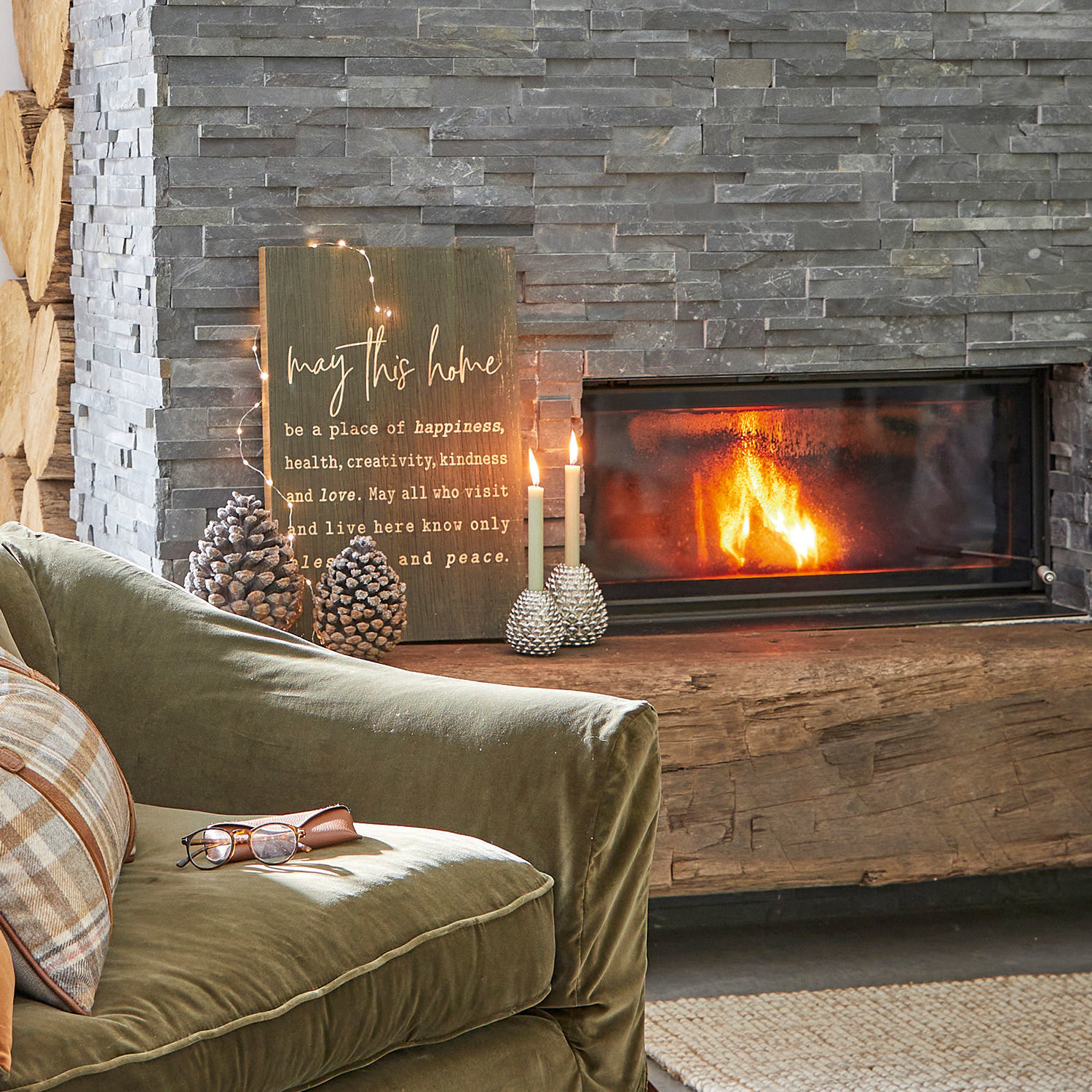 Gemütliches Wohnzimmer mit grünem Samtsofa, Steinkamin und Holz- sowie Kerzendekoration