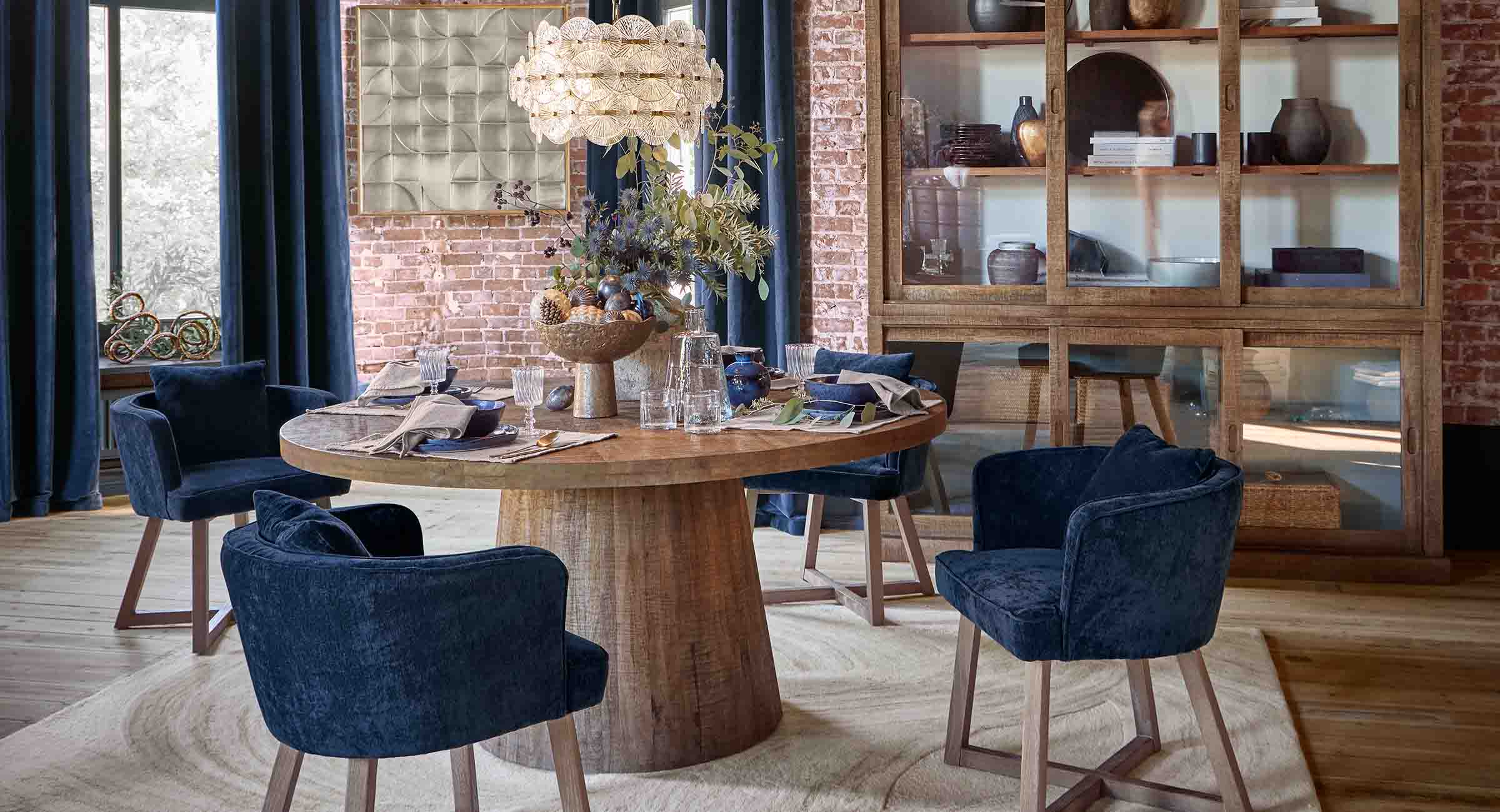 Esszimmer mit rundem Holztisch und samtblauen Stühlen im Loft-Stil mit Backsteinwand