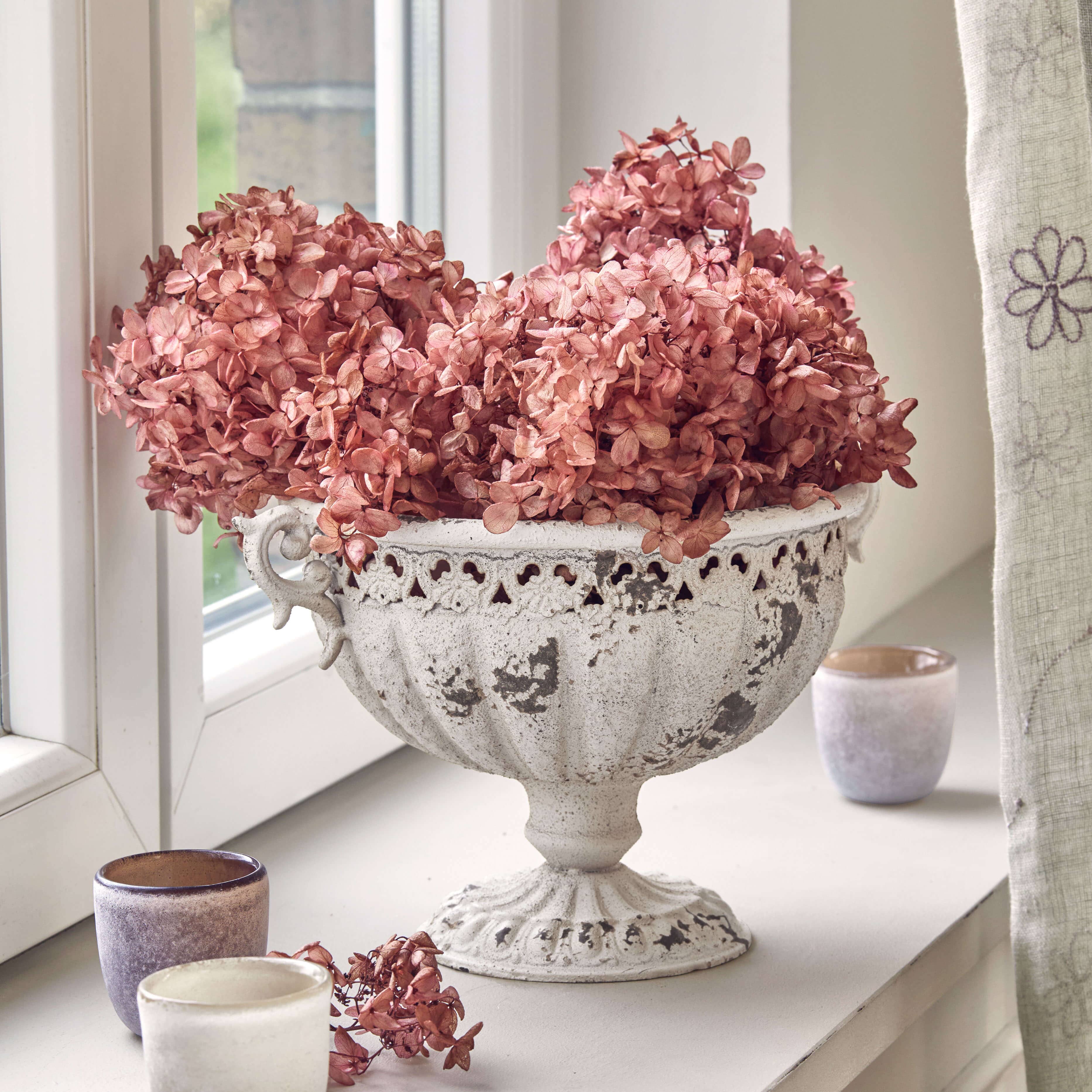 Weiße Metall-Schale mit Vintage-Finish und getrockneten rosa Blüten auf Fensterbank