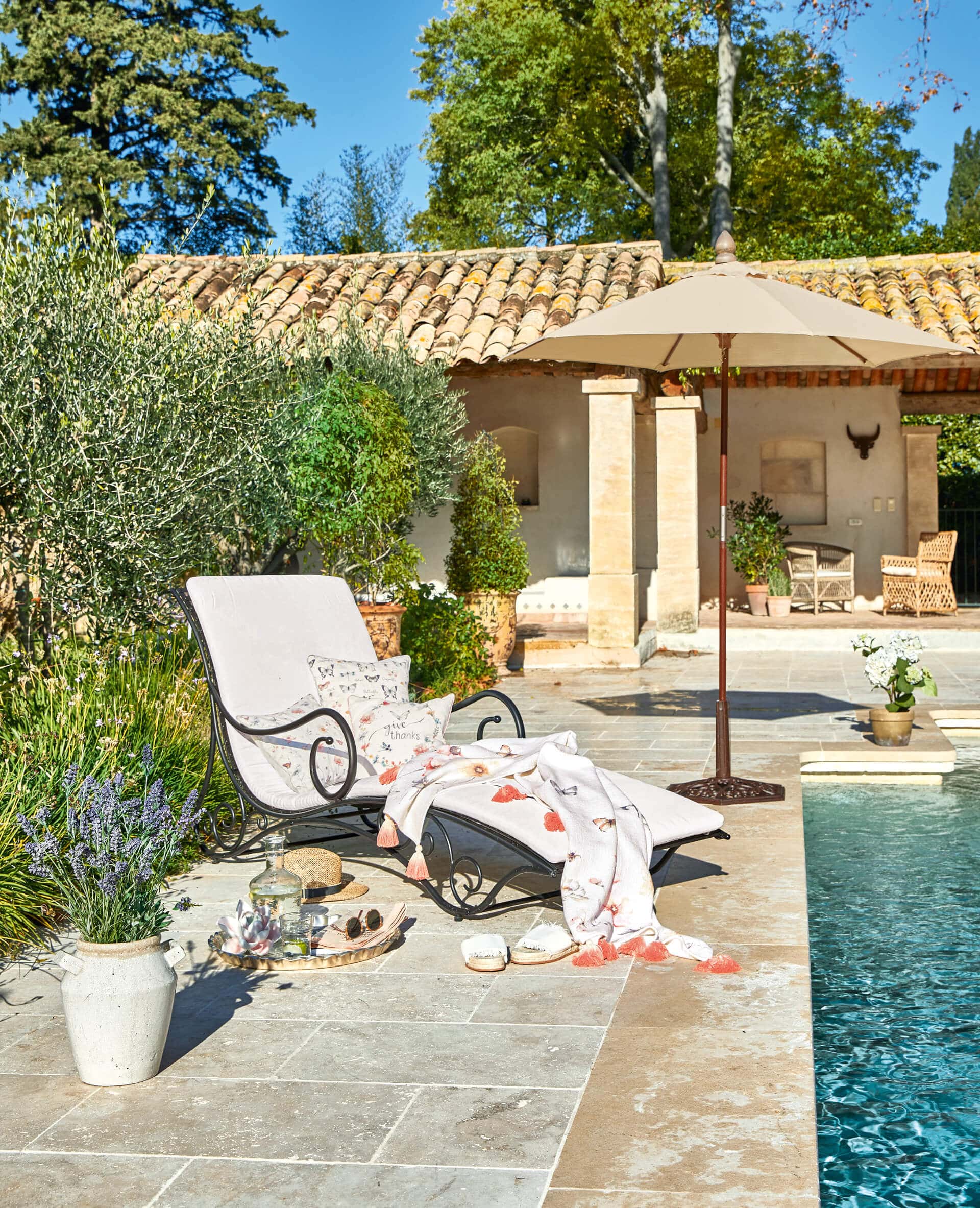 Gartenliege mit Metallrahmen und hellem Polster am Pool auf sonniger Terrasse mit Sonnenschirm