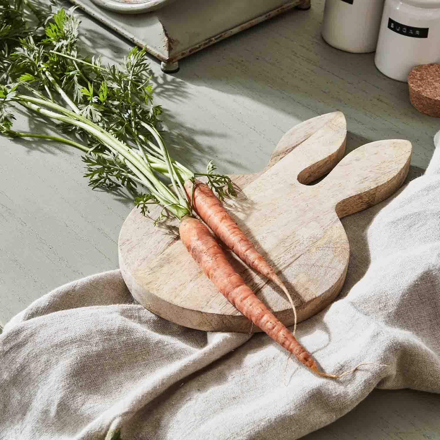Holzschneidebrett in Hasenform mit zwei frischen Karotten auf einem Leinentuch