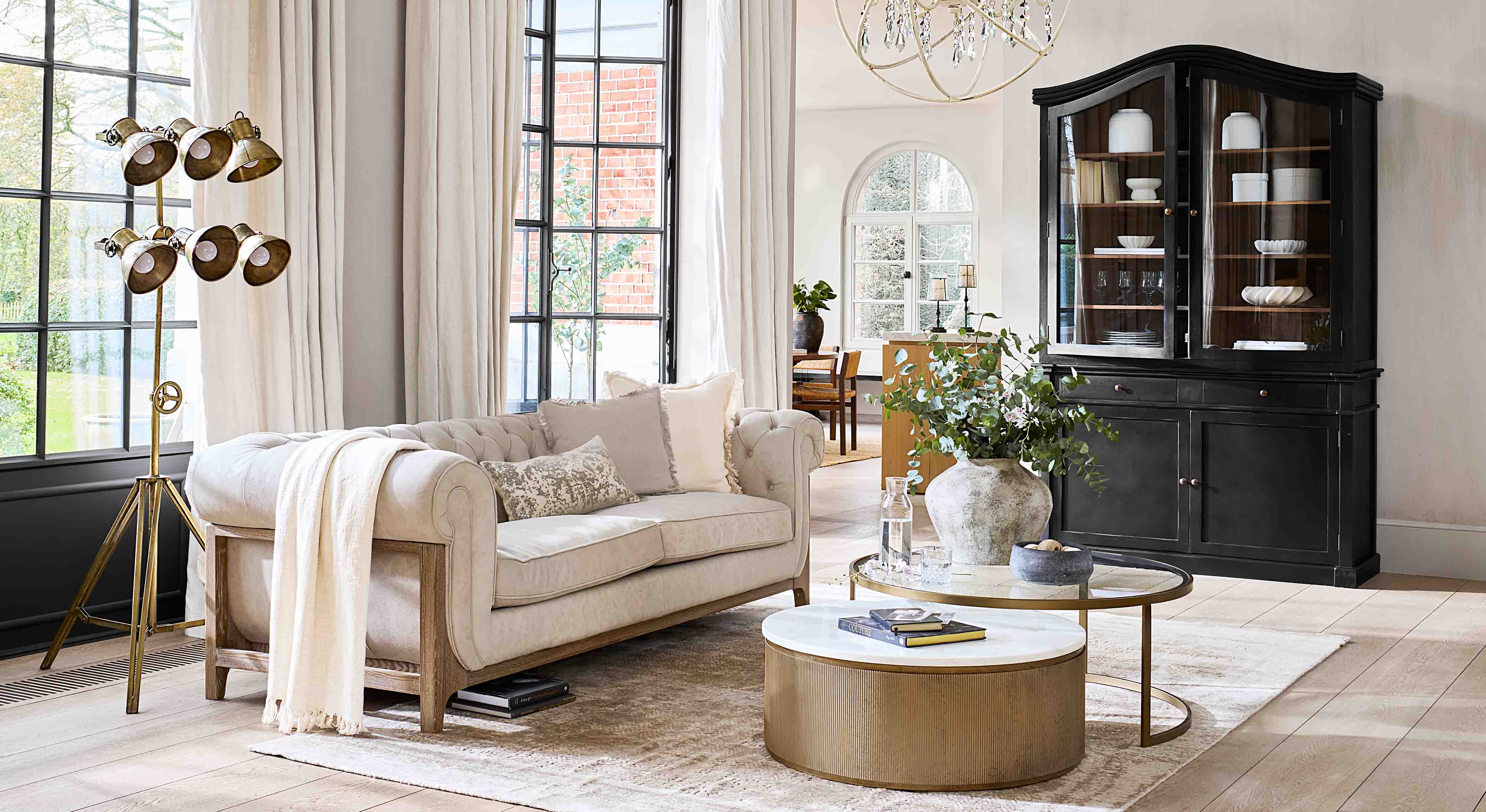 Beiges Sofa mit Holzrahmen in hellem Wohnzimmer mit schwarzem Vitrinenschrank und goldener Stehlampe