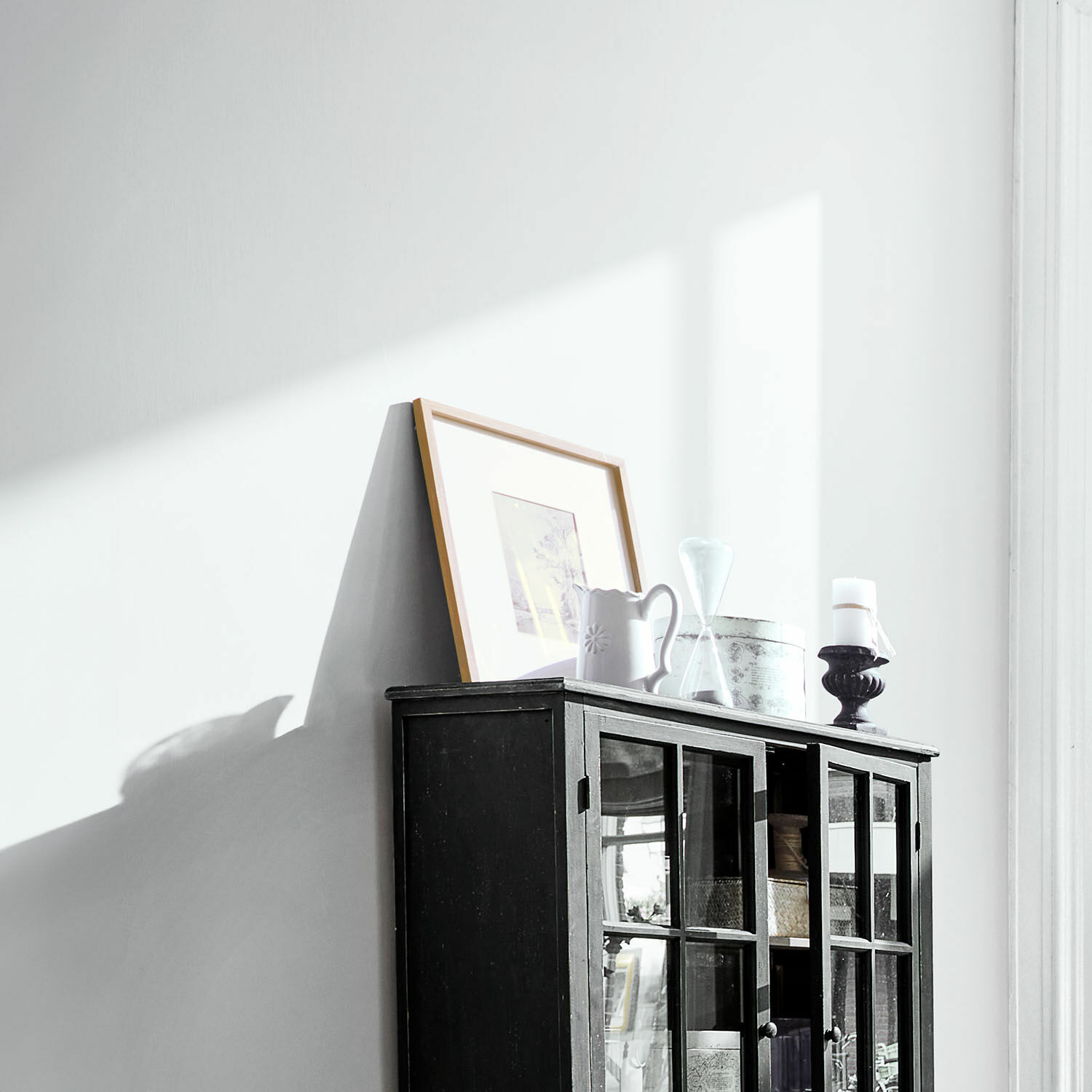 Schwarze Holzvitrine mit Glastüren und Dekorationen oben in hellem Raum