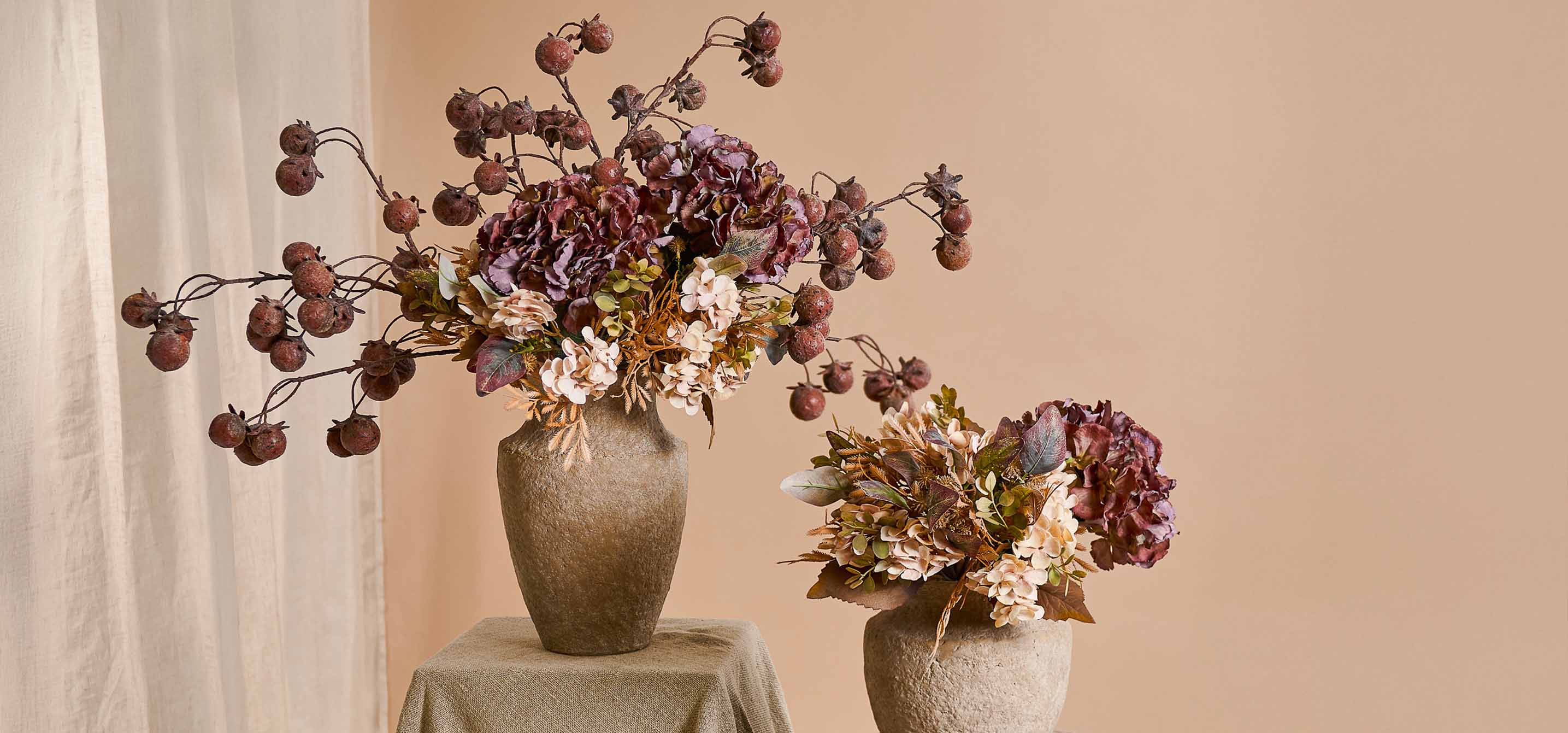 Zwei dekorative Vasen aus beigem Stein mit künstlichen Blumensträußen und Früchten in warmen Farben