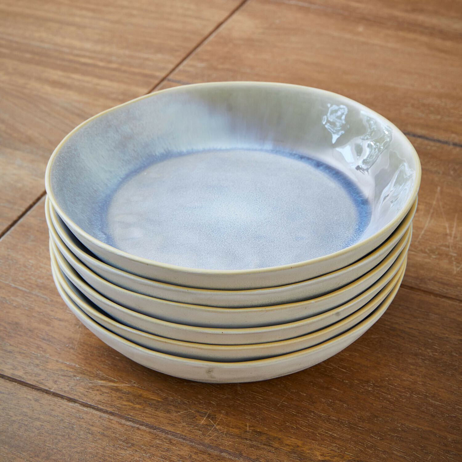 Sechsteiliges Set aus blauen und beigen Keramiktellern auf Holztisch gestapelt