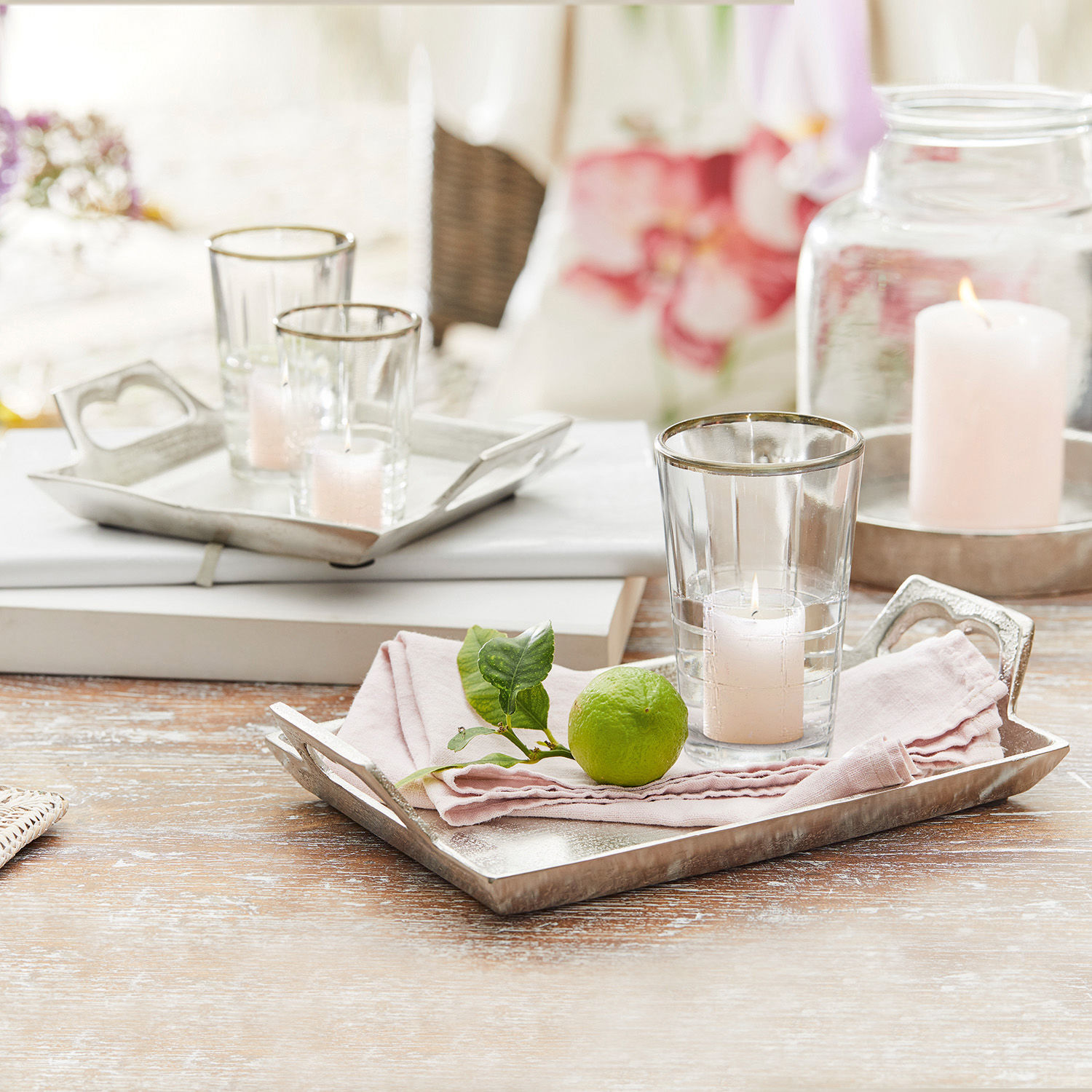 Dekoratives Metalltablett mit rosa Leinentuch, Kerze und Limette auf Holztisch