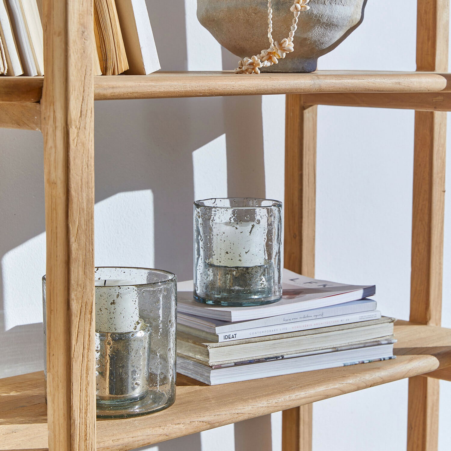Zwei Glaswindlichter mit weißen Kerzen auf Holzregal mit Büchern, Wohnaccessoire