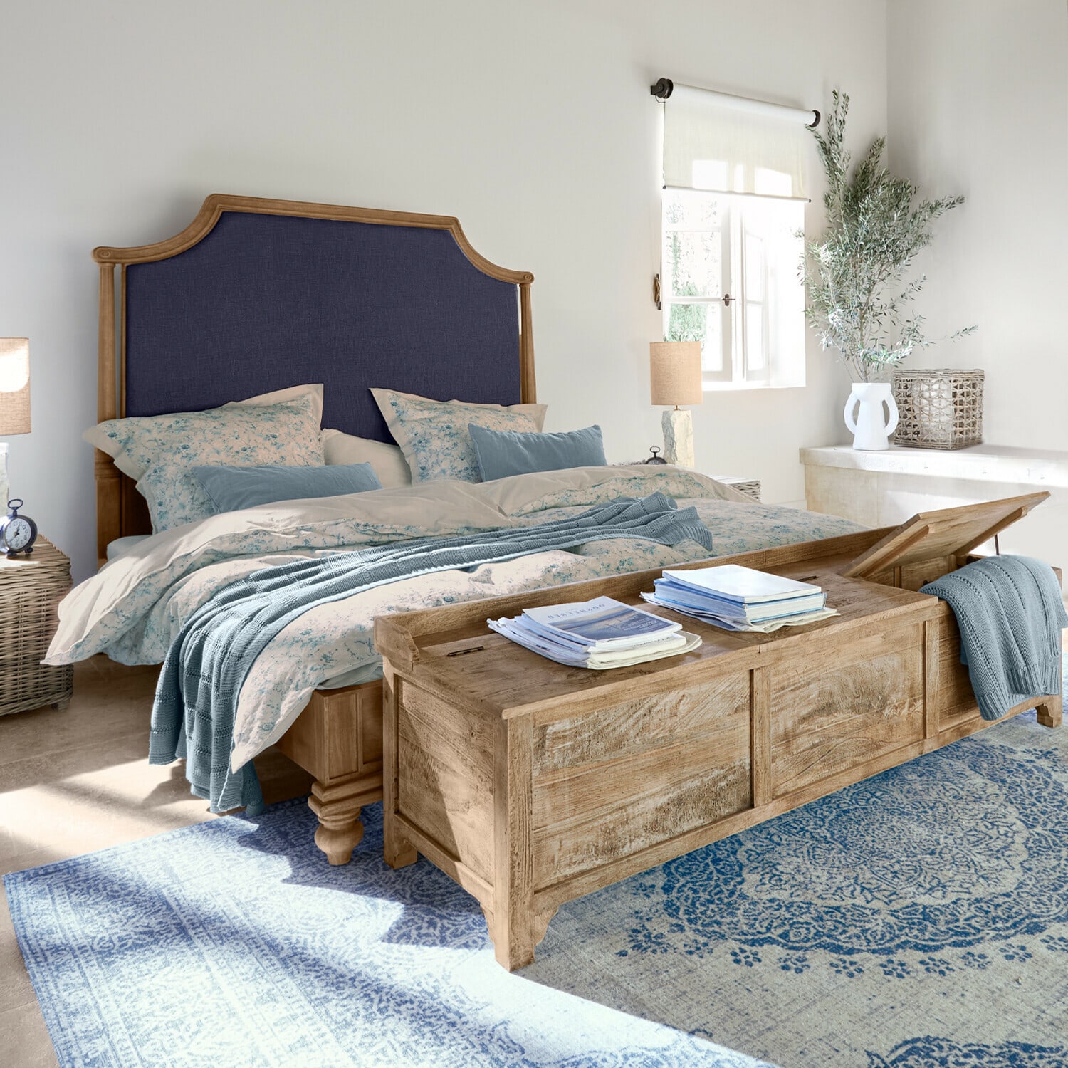 Schlafzimmer mit Holzbett, dunkelblau gepolstertem Kopfteil, blauem Teppich und passender Bettwäsche