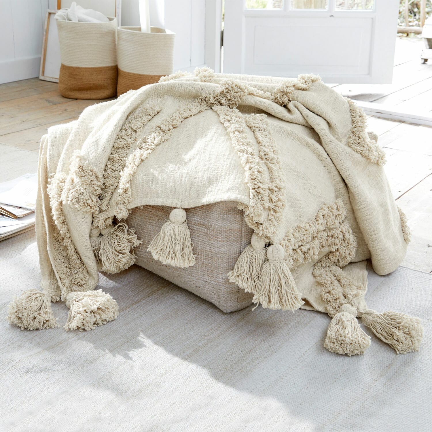 Plaid Linares Beige Baumwolldecke mit Quasten auf hellem Pouf in natürlichem, hellem Raum