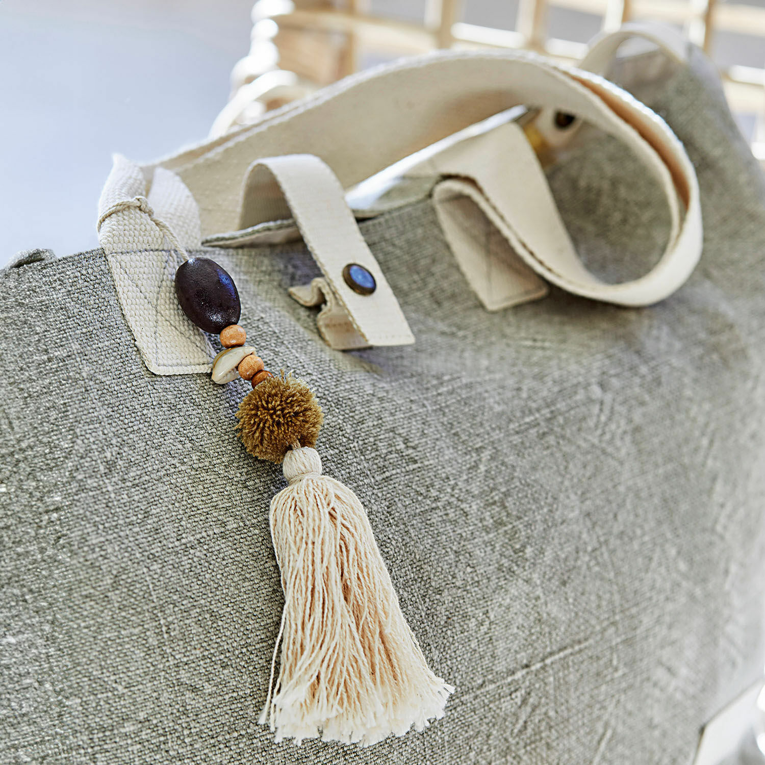 Beige Stofftasche mit dekorativem Quastenanhänger und Holzperlen, modisches Accessoire für den Alltag