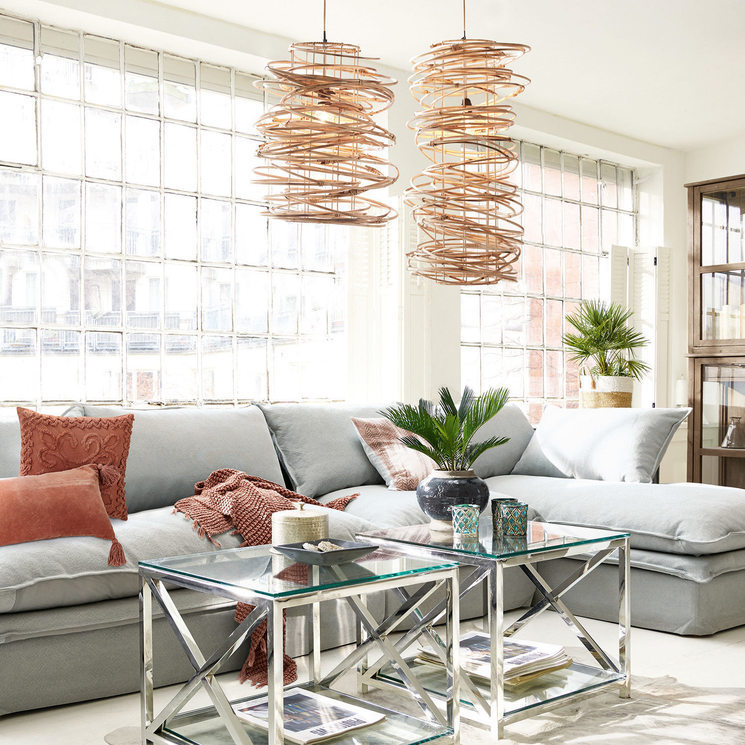 Hellgraues Ecksofa mit weichen Kissen und gläsernen Couchtischen in modernem, lichtdurchflutetem Wohnzimmer