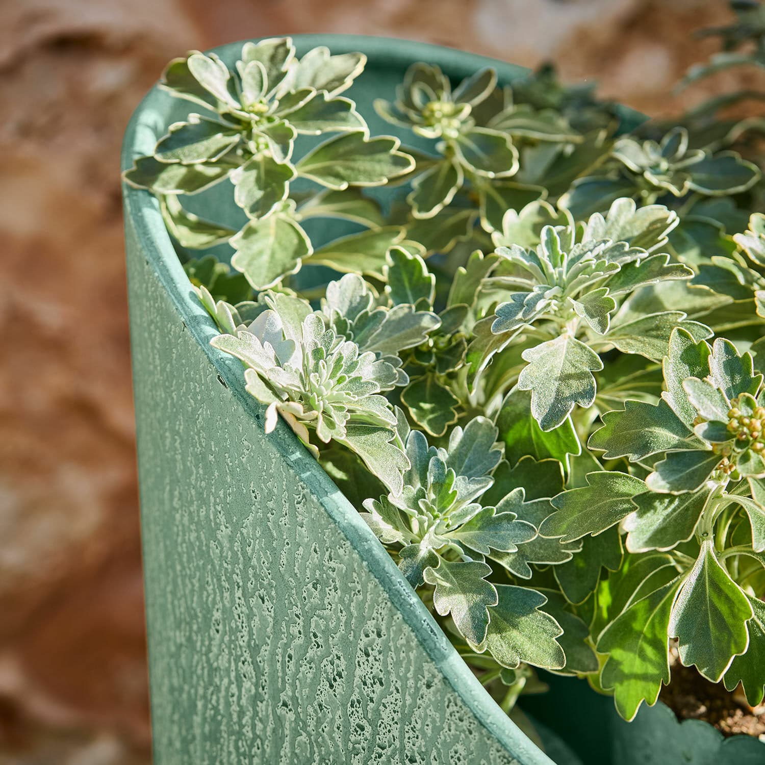 Grüner Metall-Blumentopf mit strukturierter Oberfläche und grünen Blättern, Gartendekoration
