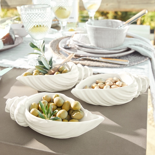 Weiße Keramikschalen in Muschelform mit Oliven und Nüssen auf Gartentisch