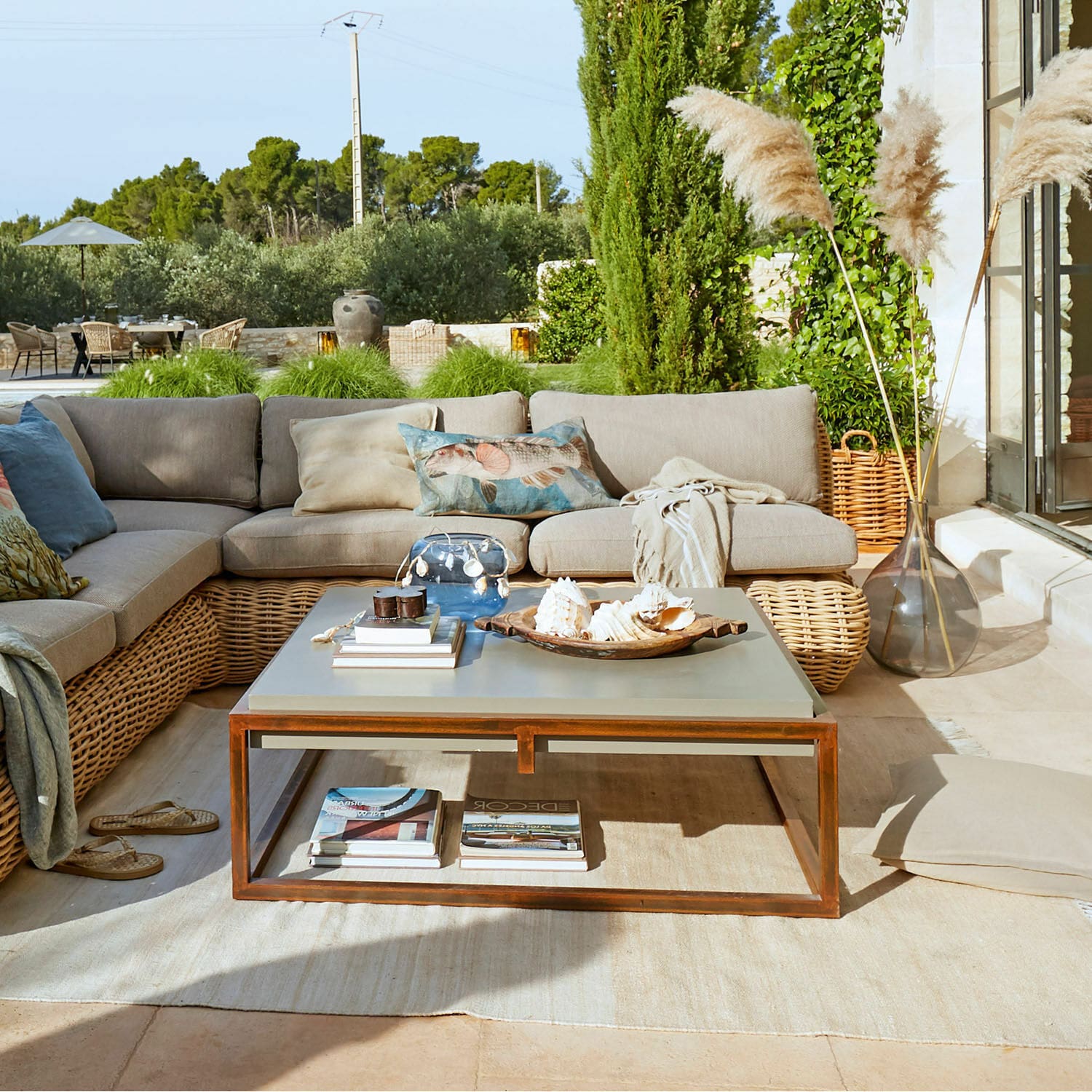 Moderner Couchtisch mit Metallrahmen und grauer Oberfläche auf Terrasse mit Rattansofa