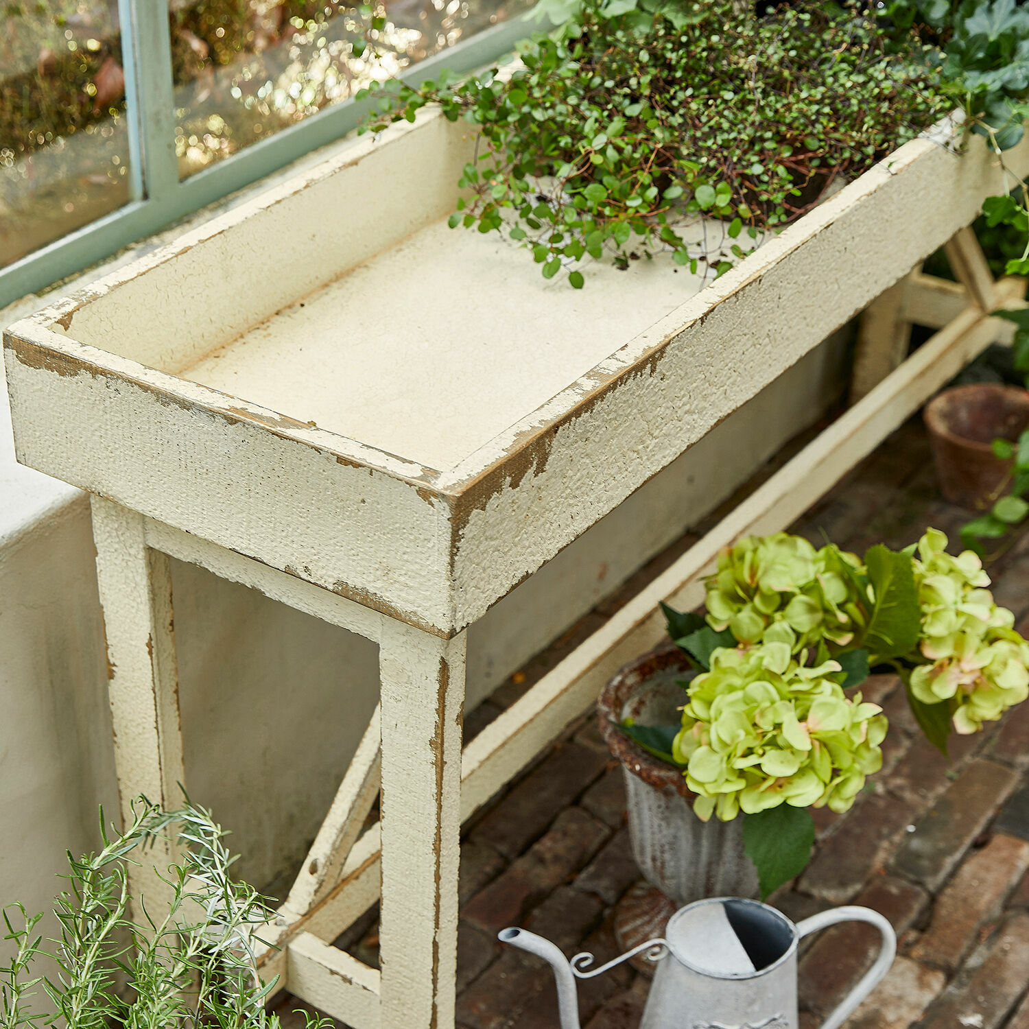 Weißer Holzgartentisch mit antiker Oberfläche und grünen Pflanzen auf Backstein-Terrasse