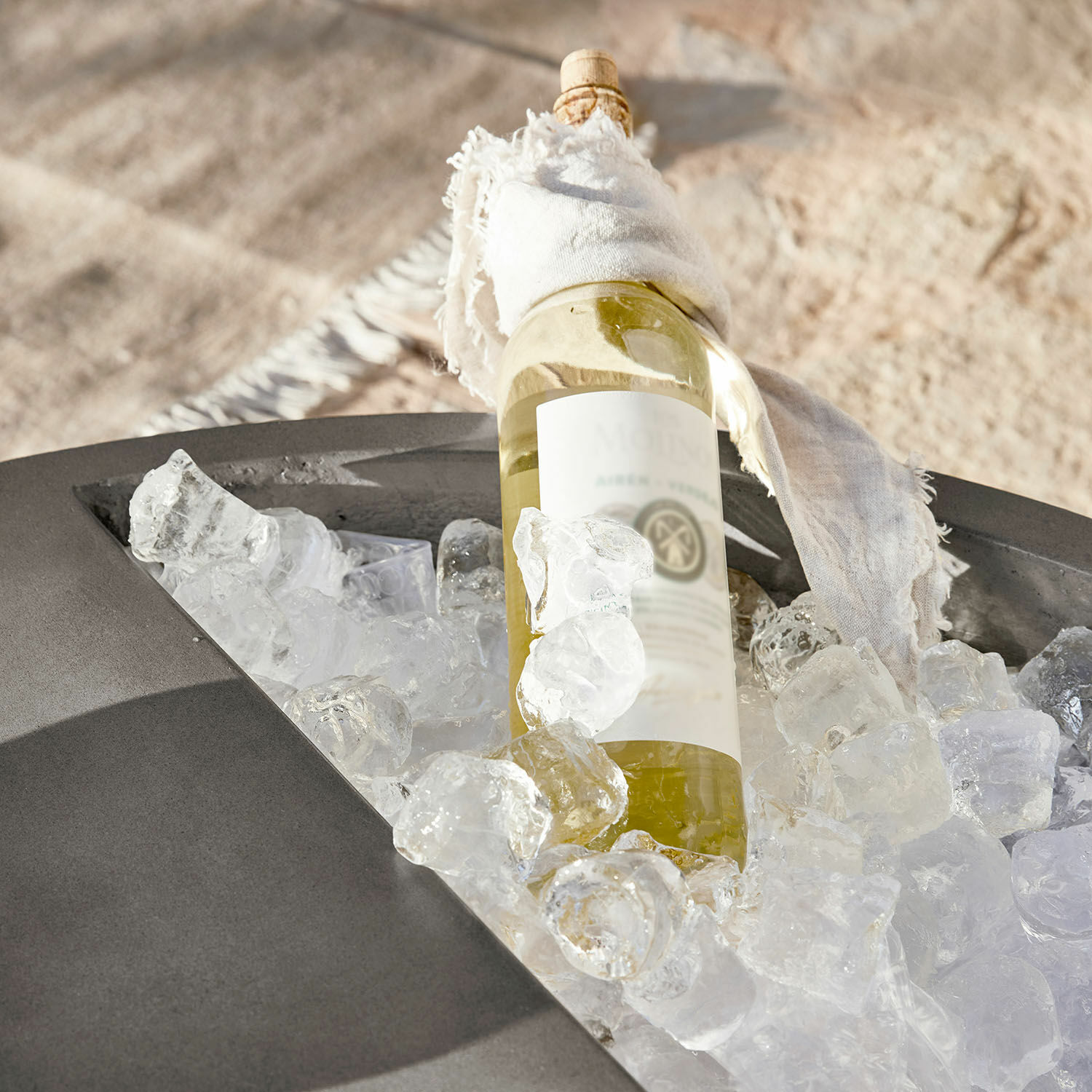 Flasche Weißwein mit weißem Tuch auf Eis in grauem Außenbehälter gekühlt