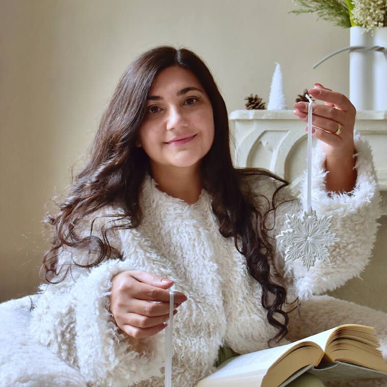Frau in weißem flauschigem Pullover hält weißen Schneeflocken-Weihnachtsschmuck mit offenem Buch am Schoß