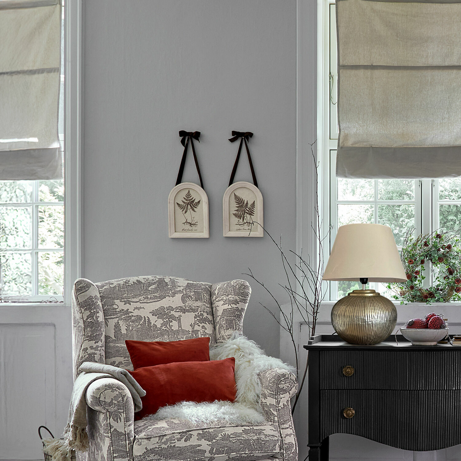 Bequemer Sessel mit grau-beigem Muster, roten Kissen und schwarzer Kommode mit Vintage-Lampe