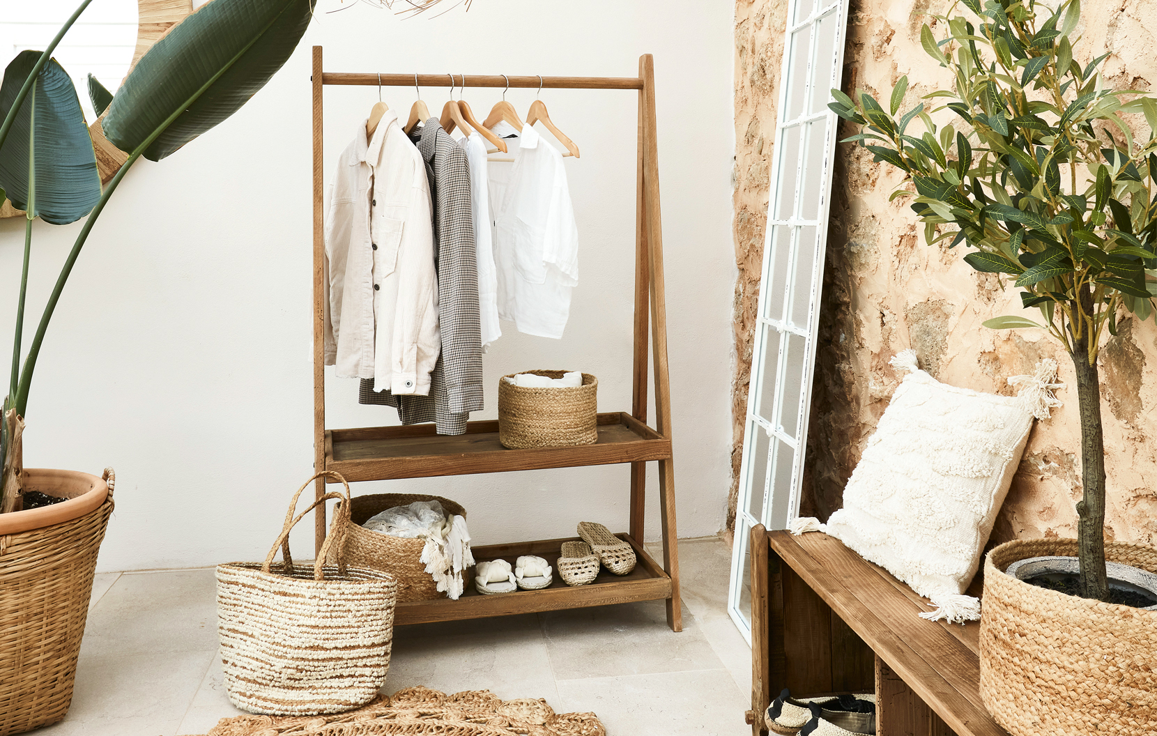 Holz-Kleiderständer mit hellen Hemden und Korb aus Weide in Boho-Wohnstil