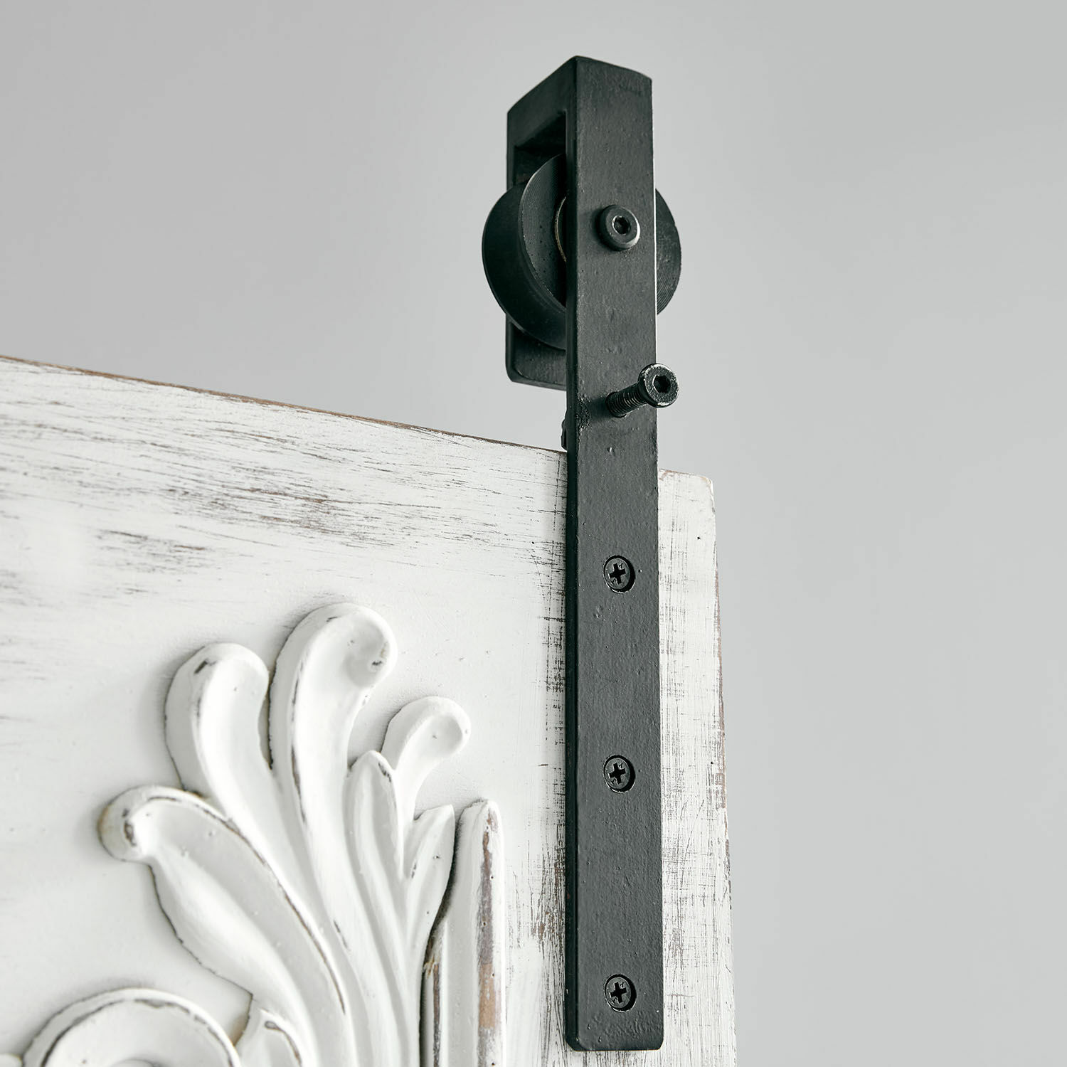 Schwarze Metall-Wandhalterung mit Rolle an weißem, antik wirkendem Türblatt mit Dekor