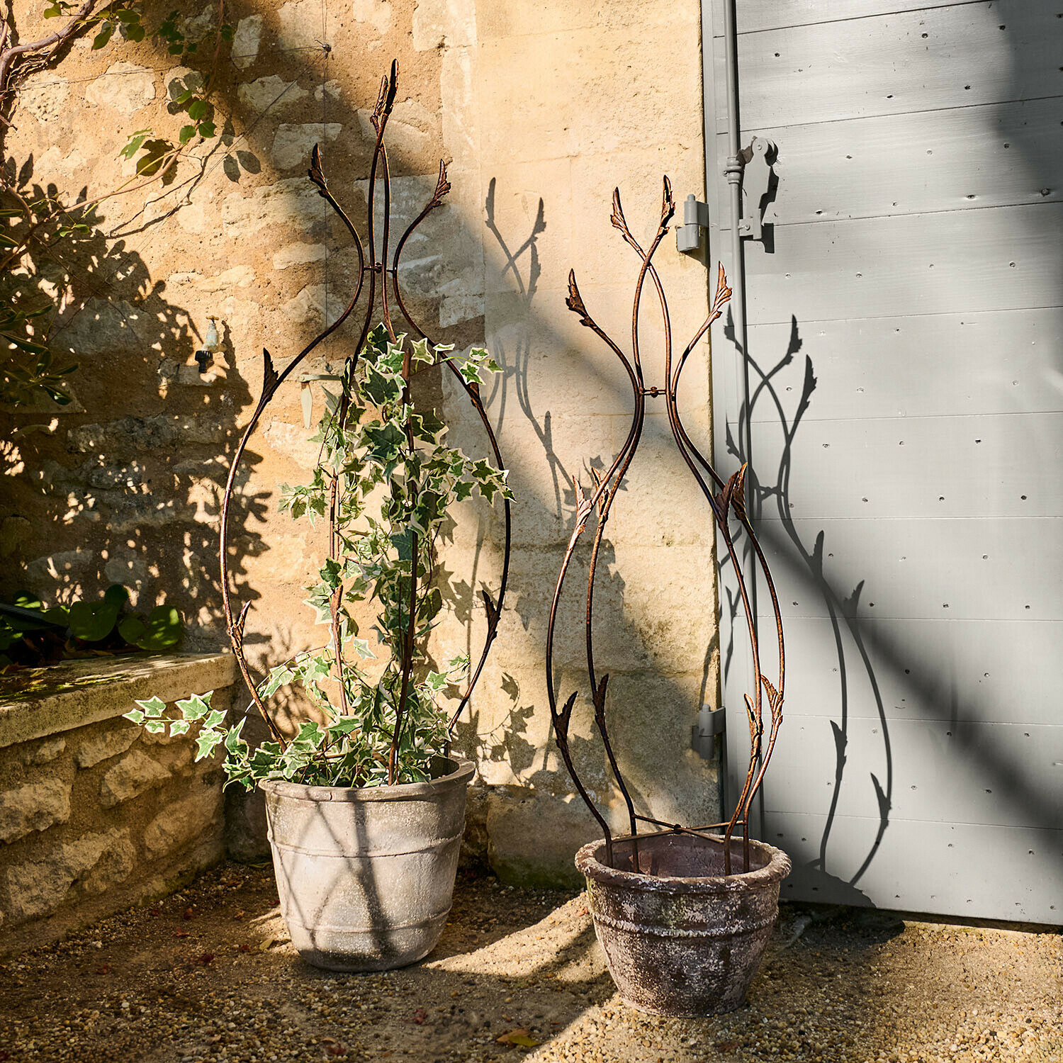 Zwei dekorative Metall-Rankhilfen in Steintöpfen auf sonniger Gartenterrasse