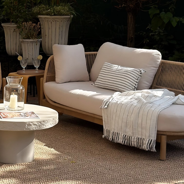 Moderne Outdoor-Sitzbank mit hellen Kissen und gestreiftem Plaid auf natürlichem Teppich im Garten