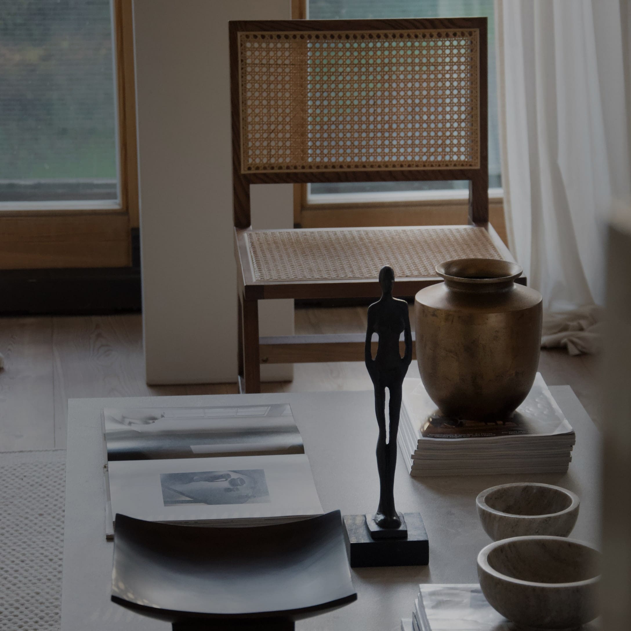 Dekorativer Tisch mit schwarzer Figur, Messingvase und Rattanstuhl im Hintergrund
