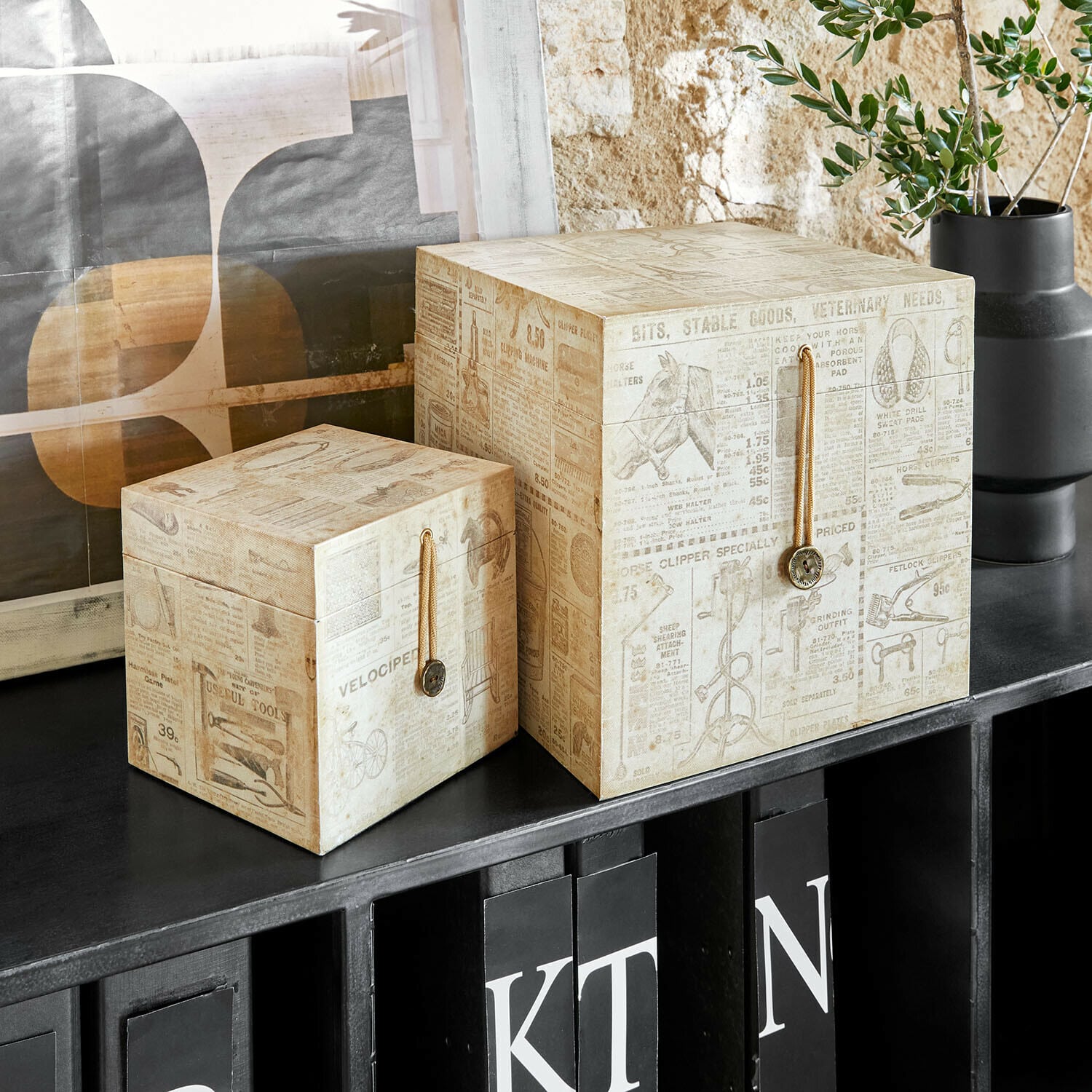 Zwei dekorative Papierboxen in Beige mit Zeitungsdruck auf schwarzem Regal