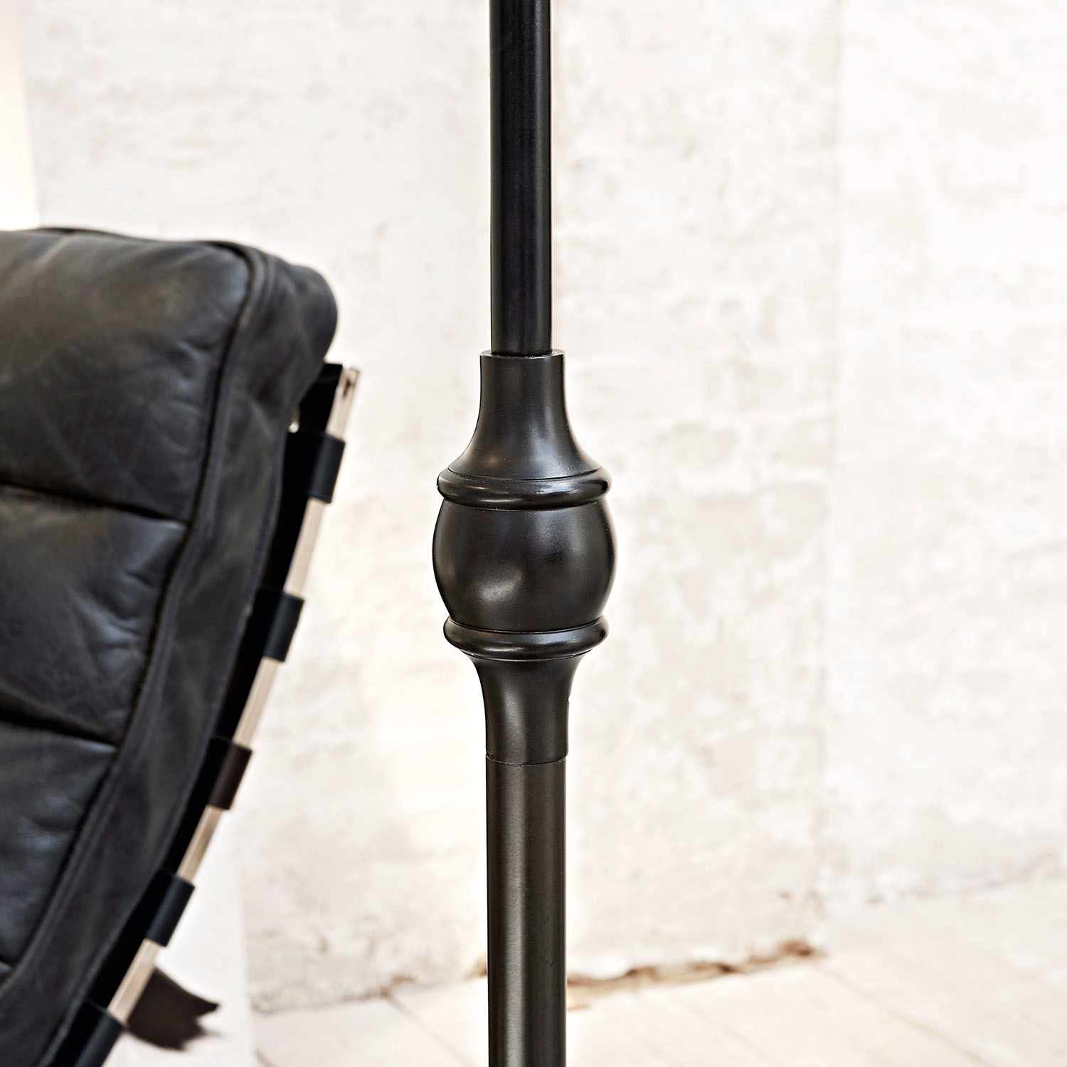 Schwarze Metall-Stehlampe mit dekorativem Detail neben schwarzem Ledersessel