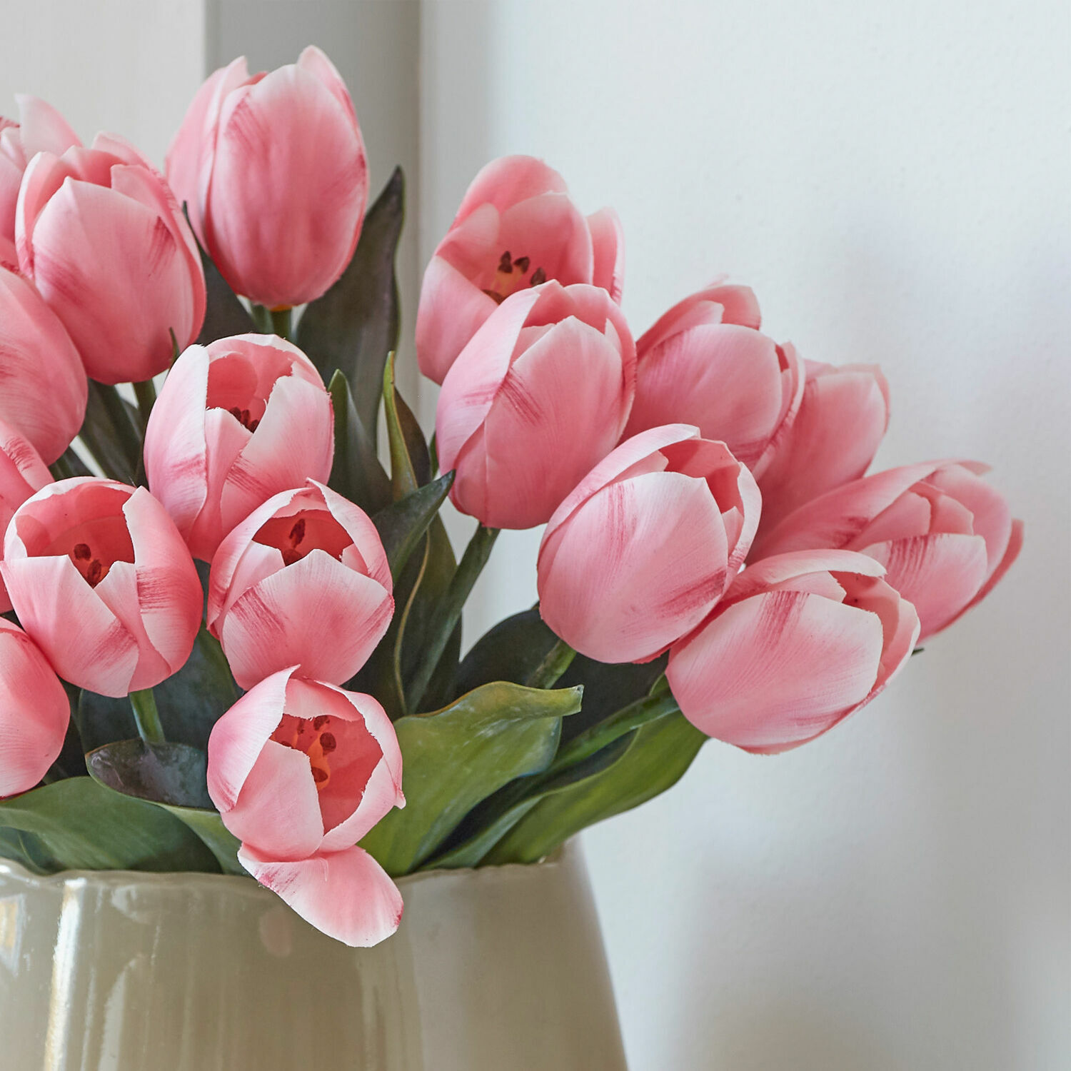 Strauß rosa Tulpen mit grünen Blättern in beiger Vase als Wohnaccessoire
