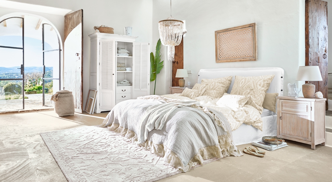 Helles Schlafzimmer mit weißem Bett, beiger Bettwäsche und rustikalen Holzmöbeln