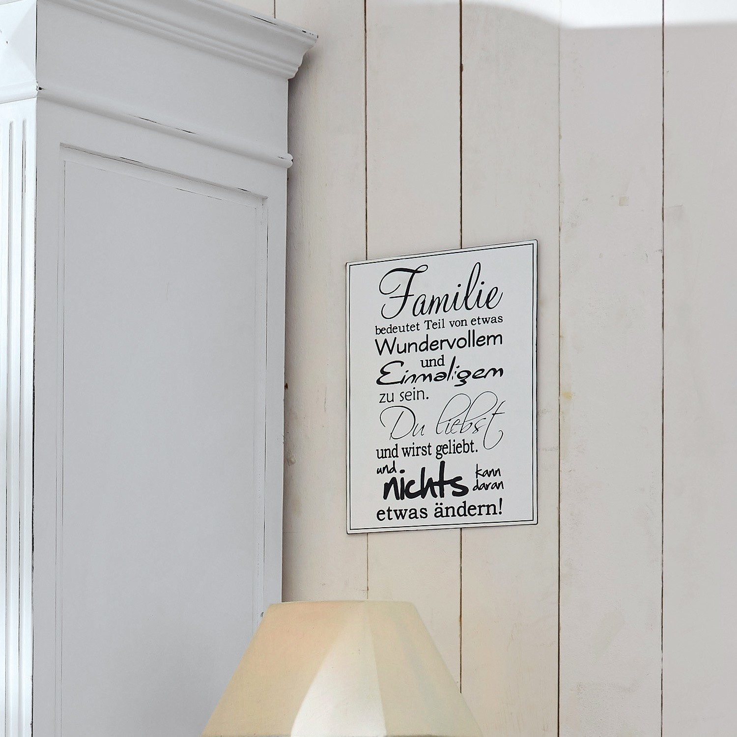 Weißes Holzschild mit Familienspruch an heller Vintage-Holzwand hängend