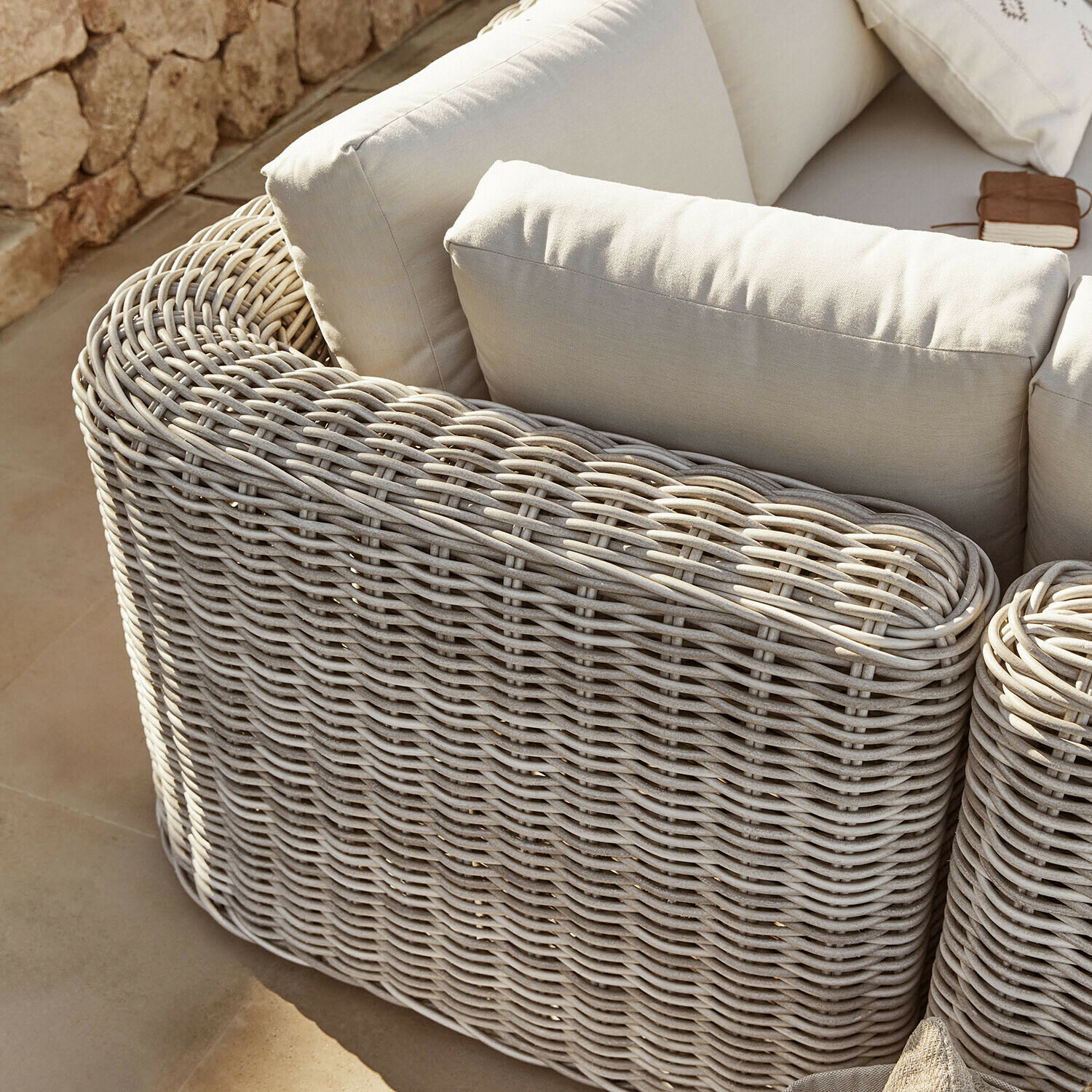 Hellgraues Rattan-Sofa mit cremefarbenen Kissen, gemütliches Outdoor-Möbel für entspannte Stunden