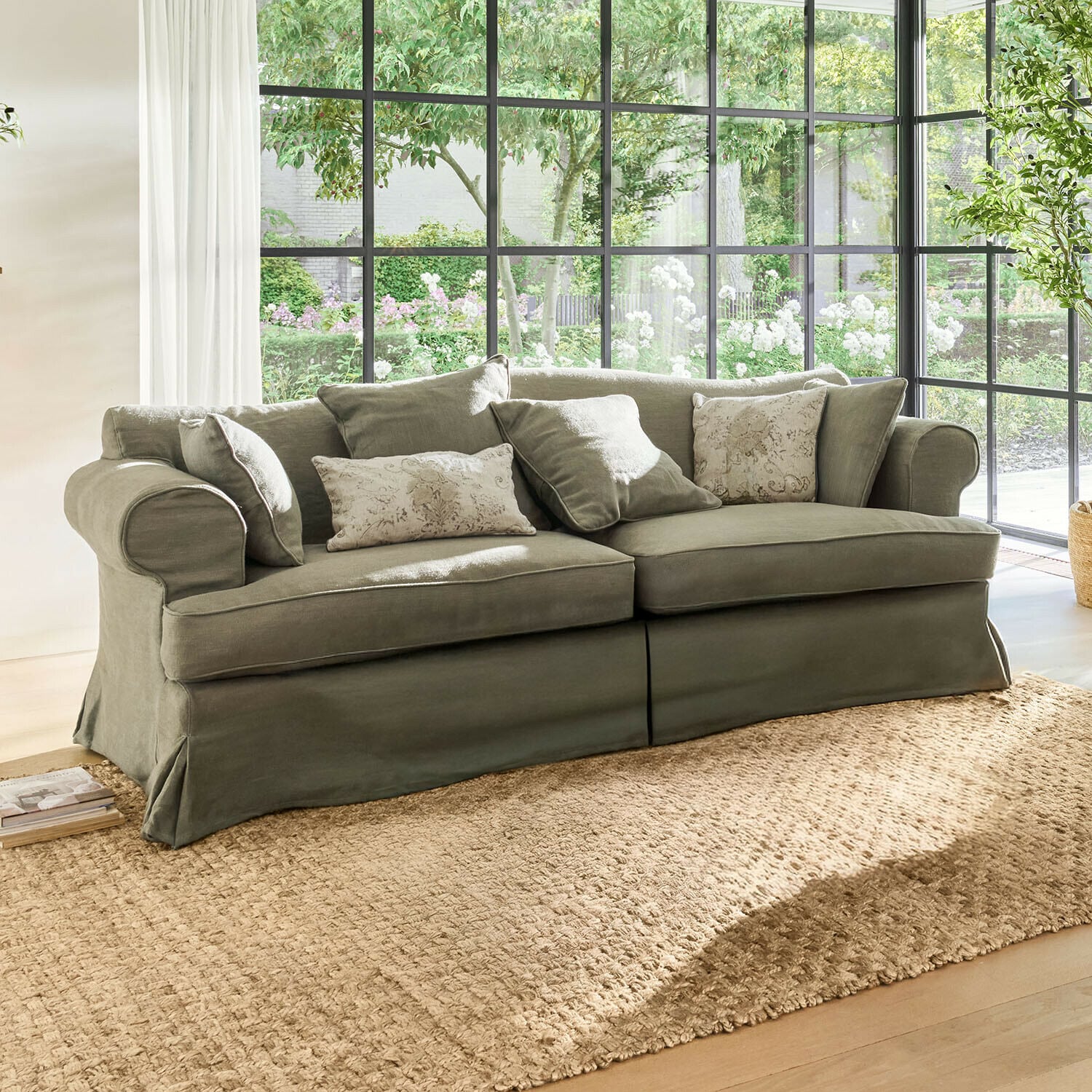 Sofa Dawnhurst Graues Sofa aus Stoff mit dekorativen Kissen vor großen Fenstern mit Tageslicht
