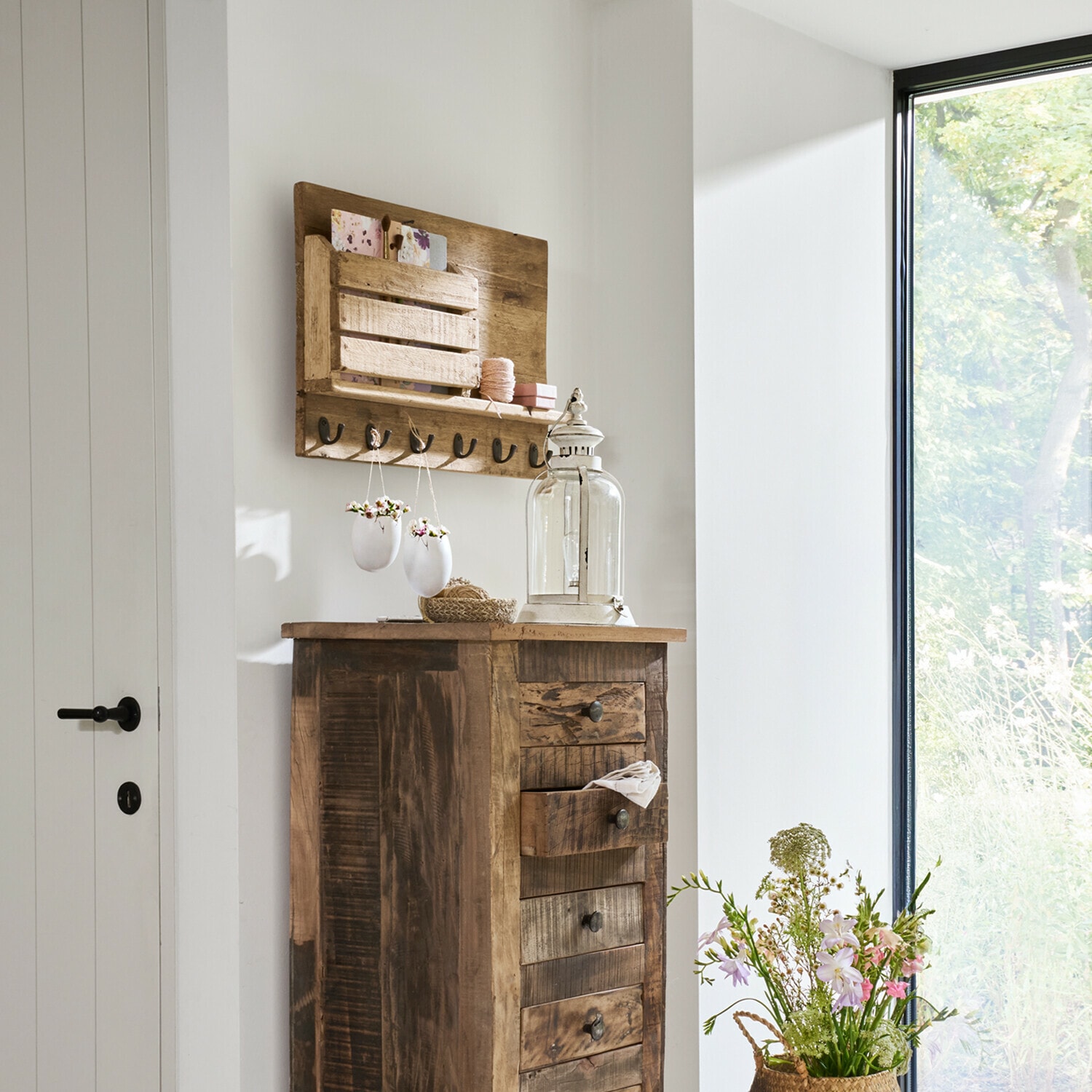 Rustikaler Holzkommode mit Schubladen und Wandhaken in hellem Raum mit Blumenarrangement