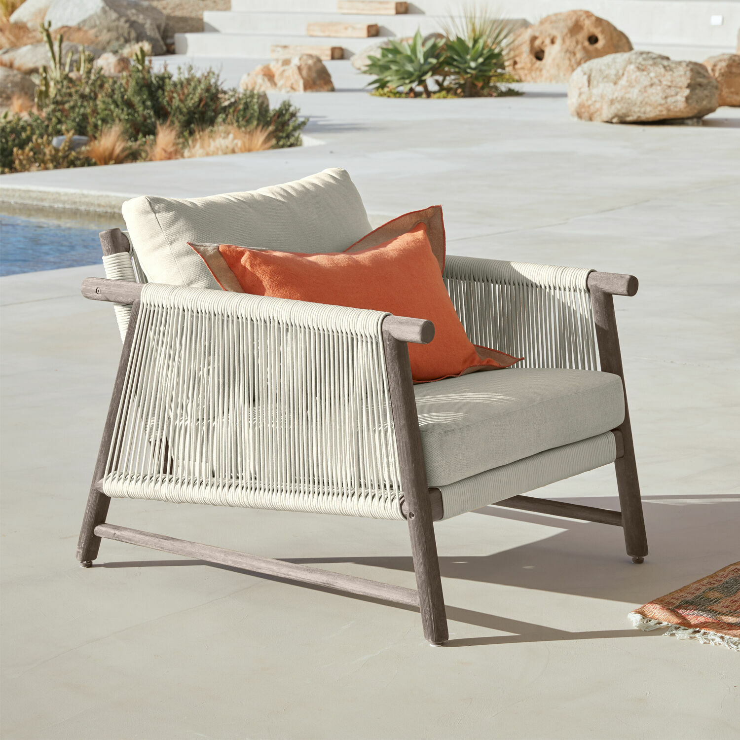 Gartenstuhl mit grauem Holzgestell, cremefarbenen Polstern und orangefarbener Dekokissen für Terrasse