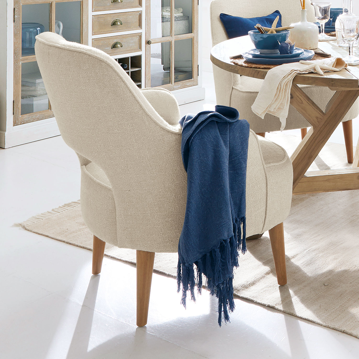 Beiger Polsterstuhl mit Holzbeinen und blauem Überwurf in hellem Wohnzimmer mit Holztisch
