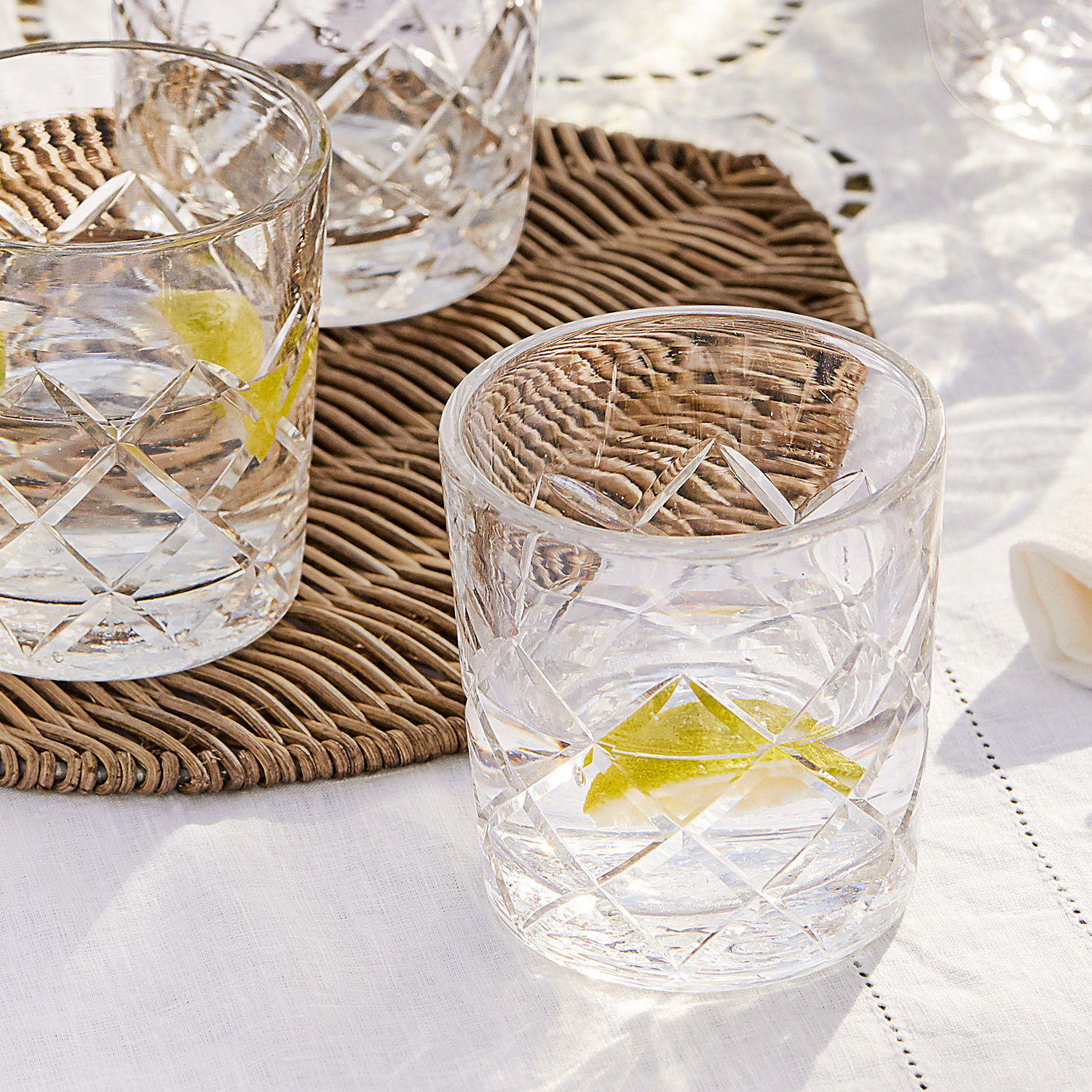 Whiskyglas aus klarem Glas mit Diamantmuster und Zitronenscheibe auf weißer Tischdecke