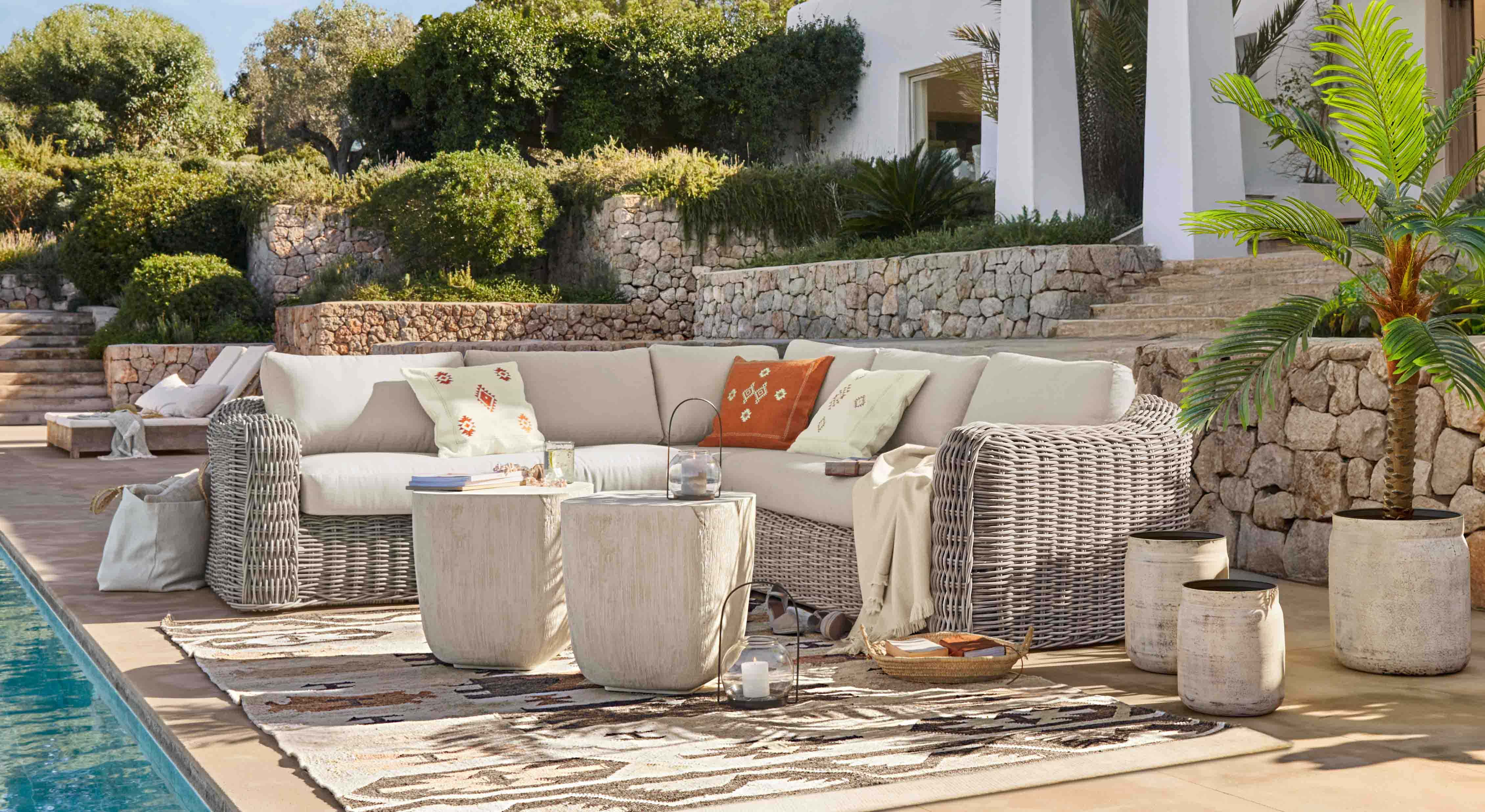 Gartenmöbel-Set aus hellgrauem Rattan mit cremefarbenen Polstern und dekorativen Kissen auf Terrasse am Pool