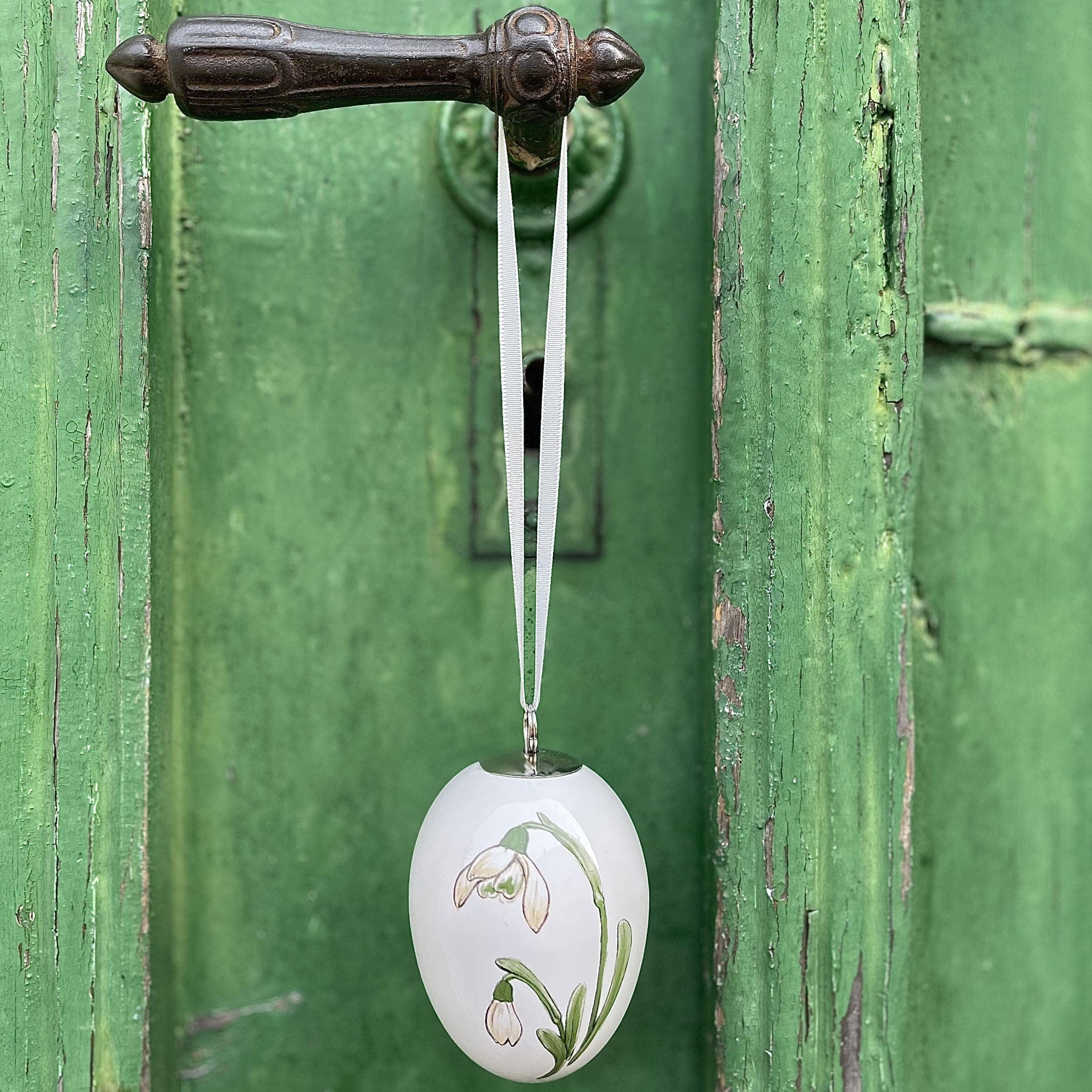 Weiße Keramik-Ostereier-Dekoration mit Blumenmotiv an grünem Türgriff hängend