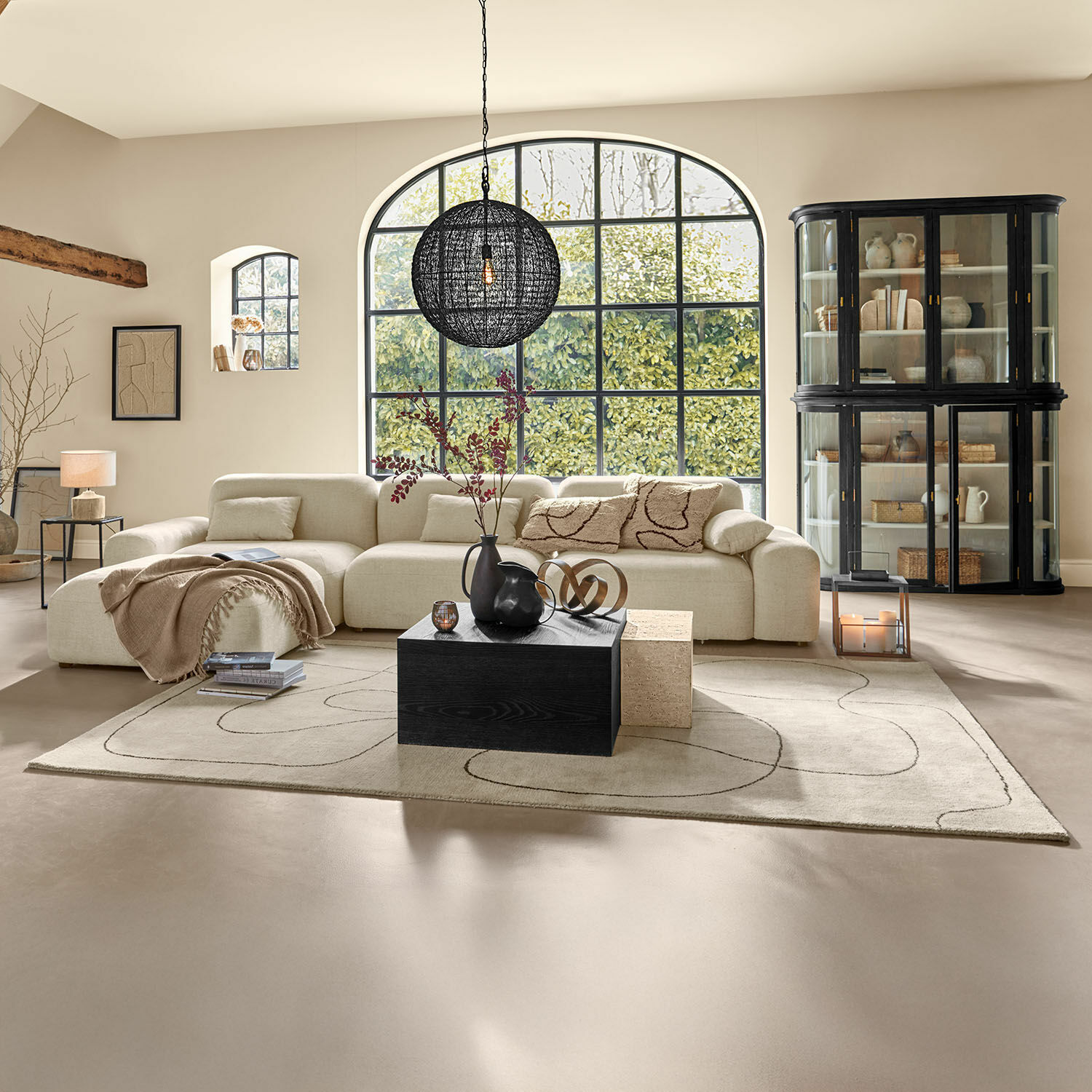 Teppich Lavinois Geräumiges Wohnzimmer mit beigem Stoffsofa, schwarzem Holztisch und großem Fenster mit Blick ins Grüne